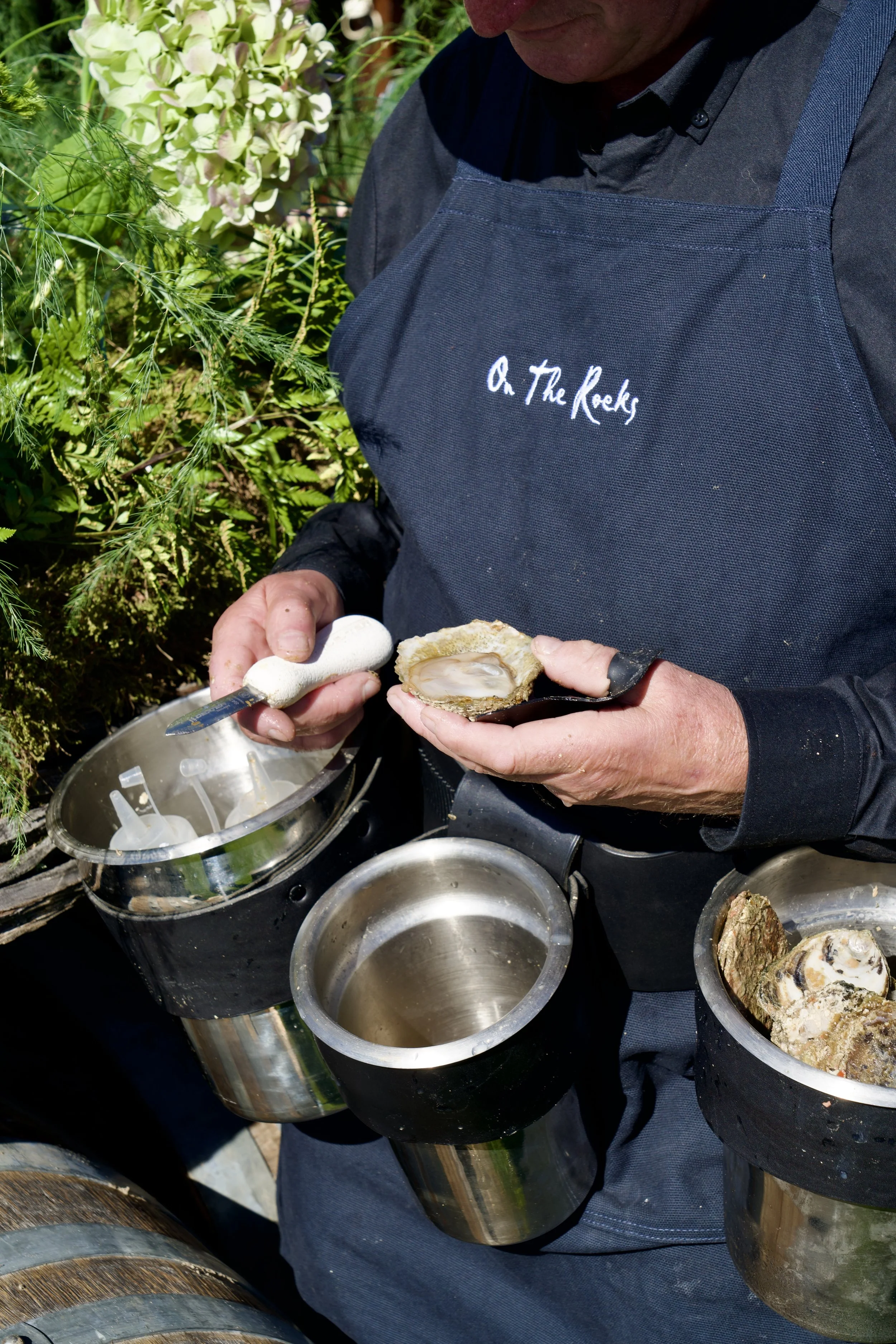 Close-up of oyster shucker opening Bluff oyster in apron with wedding florals in background