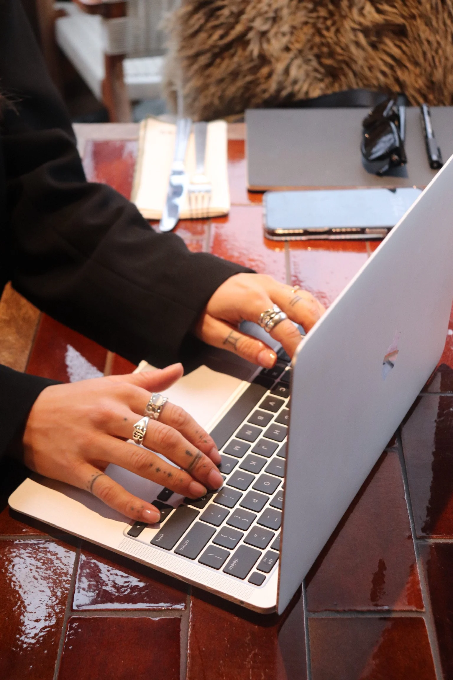 Close-up of Nicola working on MacBook Air with designer sunglasses, branded notebook, and Bowden Studio phone in the background — brand content creation workspace.