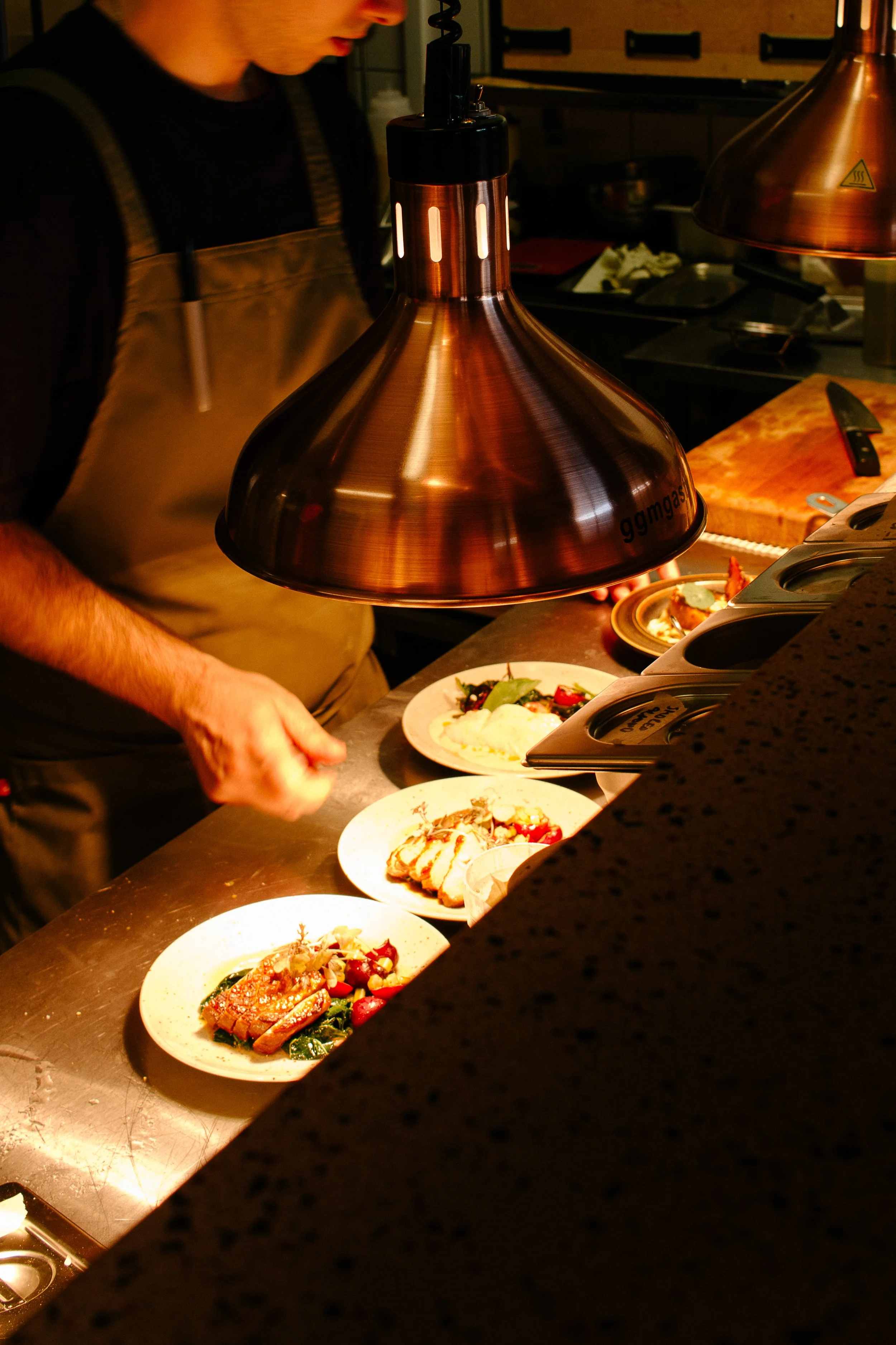 Chef placing food under heat lamp with plates of prepared dishes on counter.