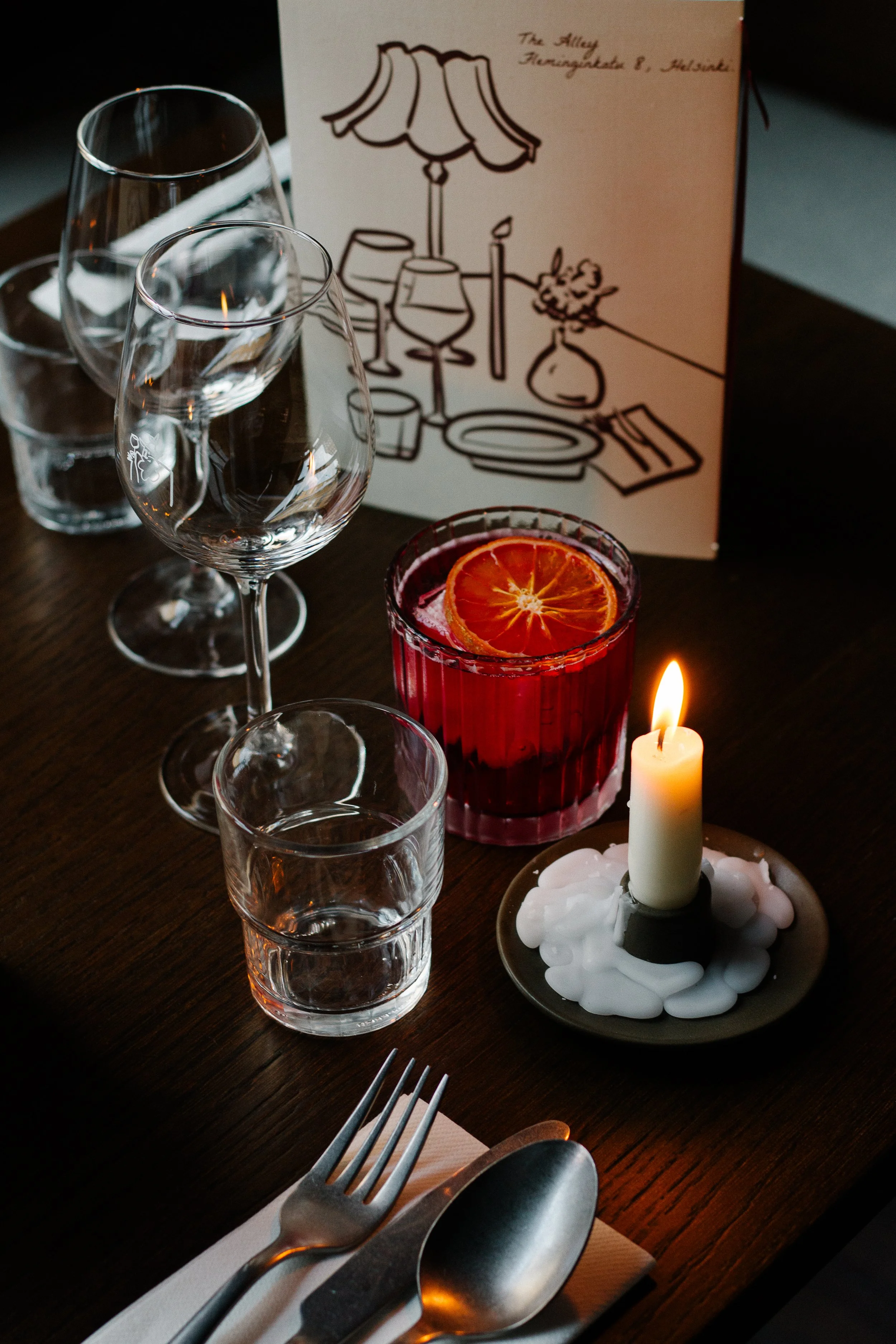 Table setting with various glasses, a candle, and a menu card in background.