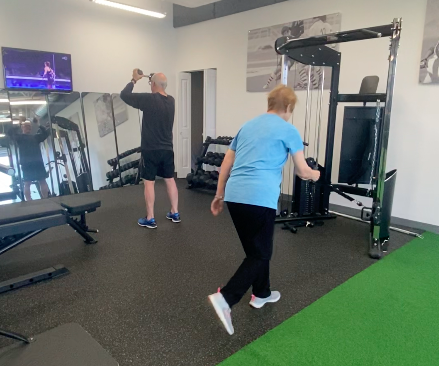 A woman is exercising on the cable machine while a man works out with dumbbells in a gym.