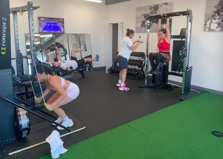 People working out in a gym, some using weight machines and others doing exercises on the floor.