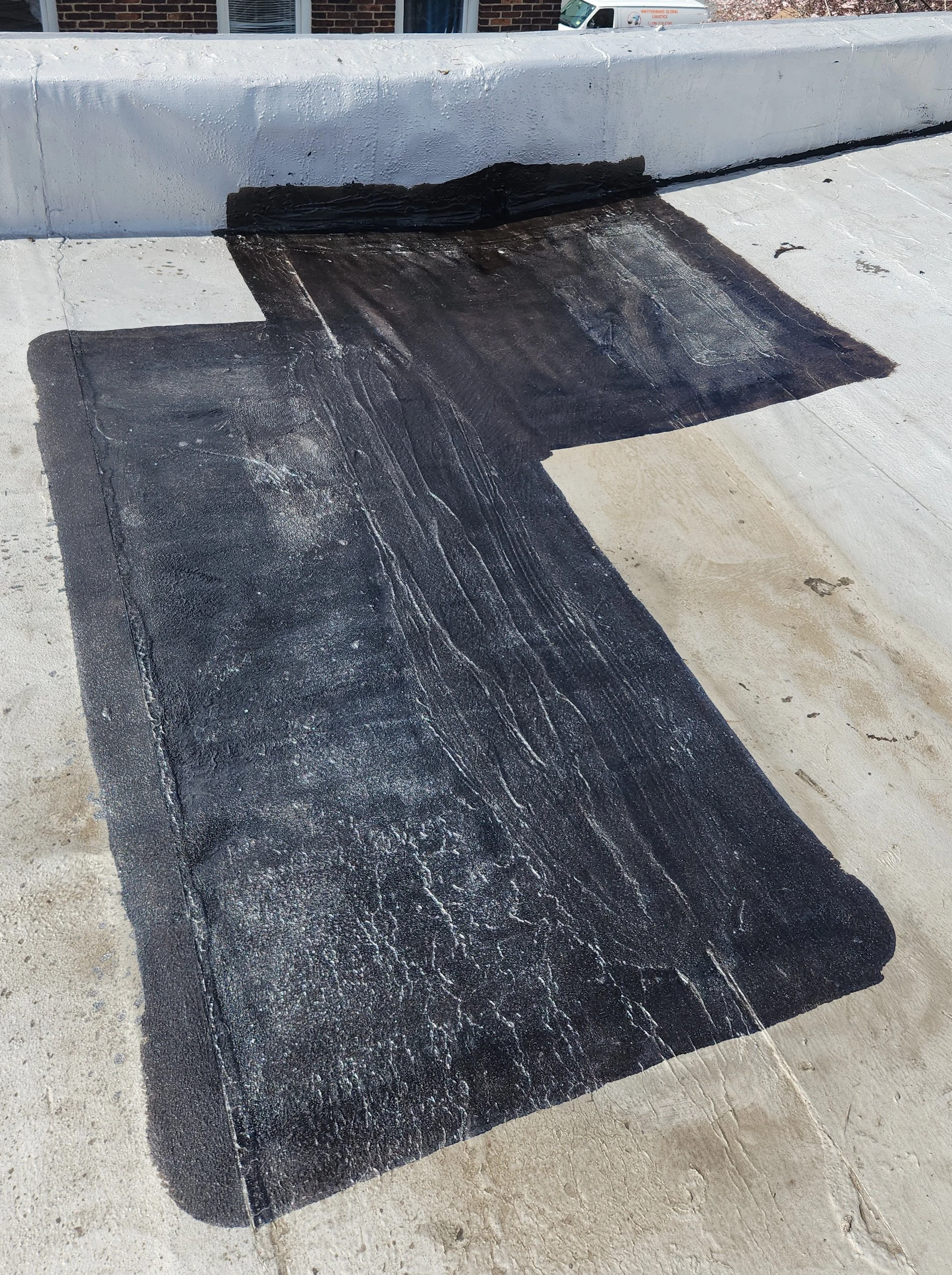 A large rectangular patch of black waterproofing membrane applied on a flat concrete roof surface, with an overhanging edge and visible seams.