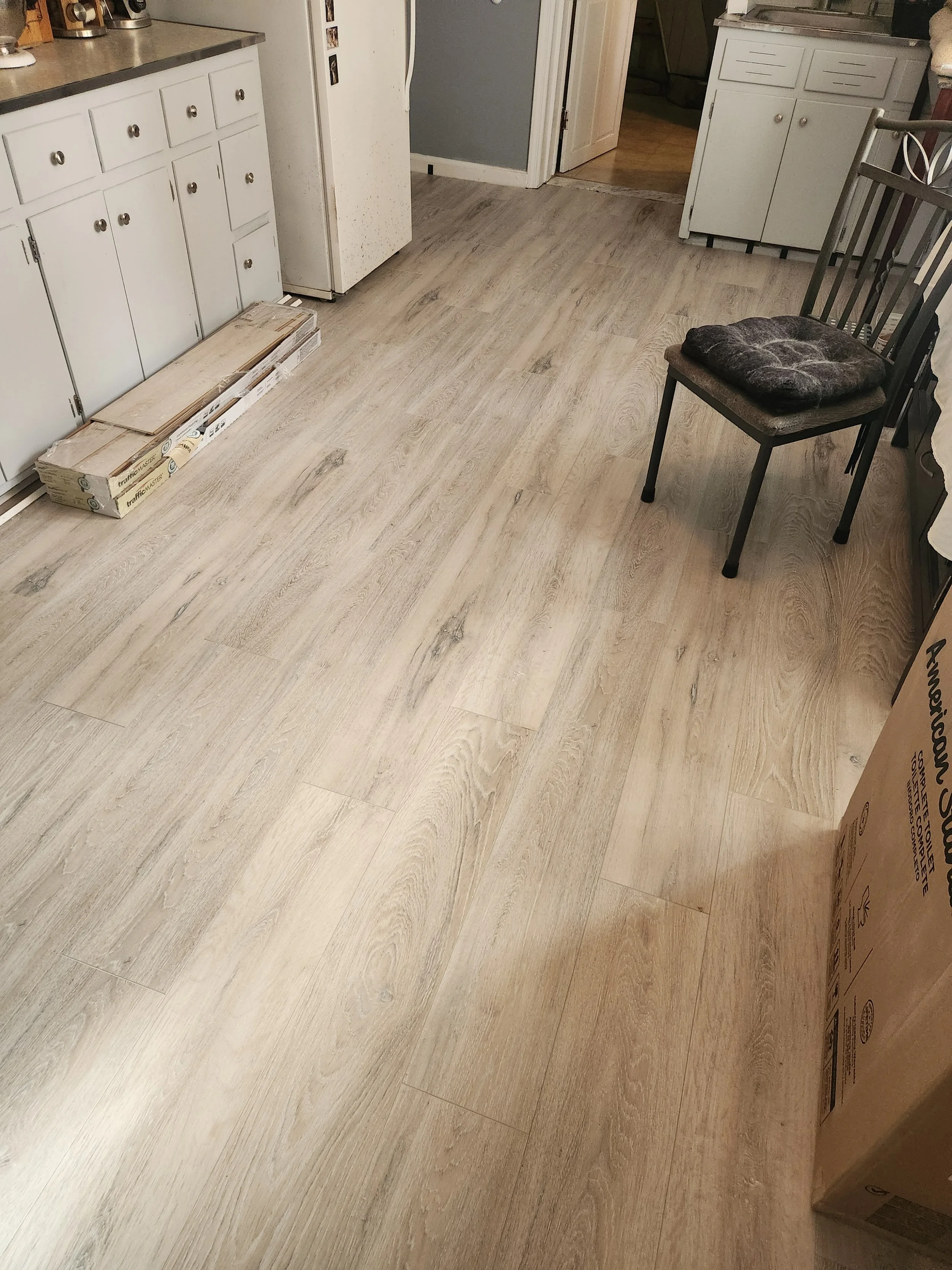 Unfinished kitchen with light wood laminate flooring, white cabinets, and a black chair with a cushion