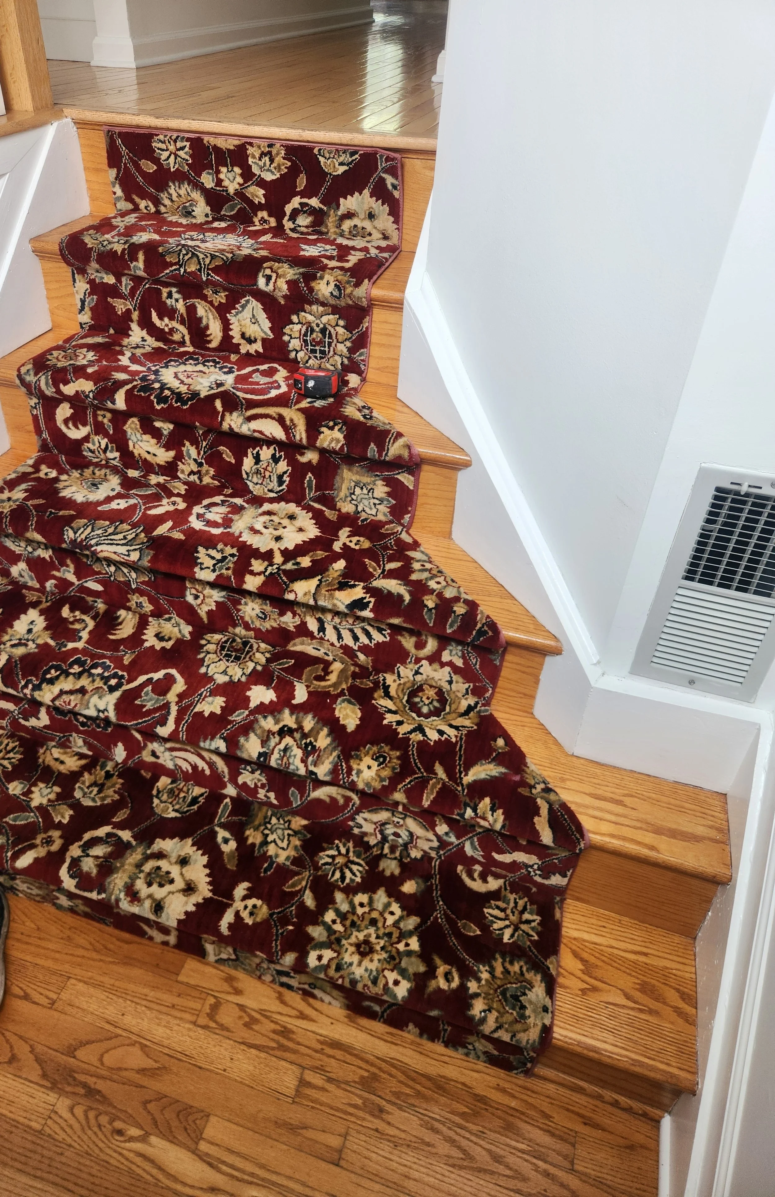 A staircase with a Persian-style rug runner and a tape measure on it.