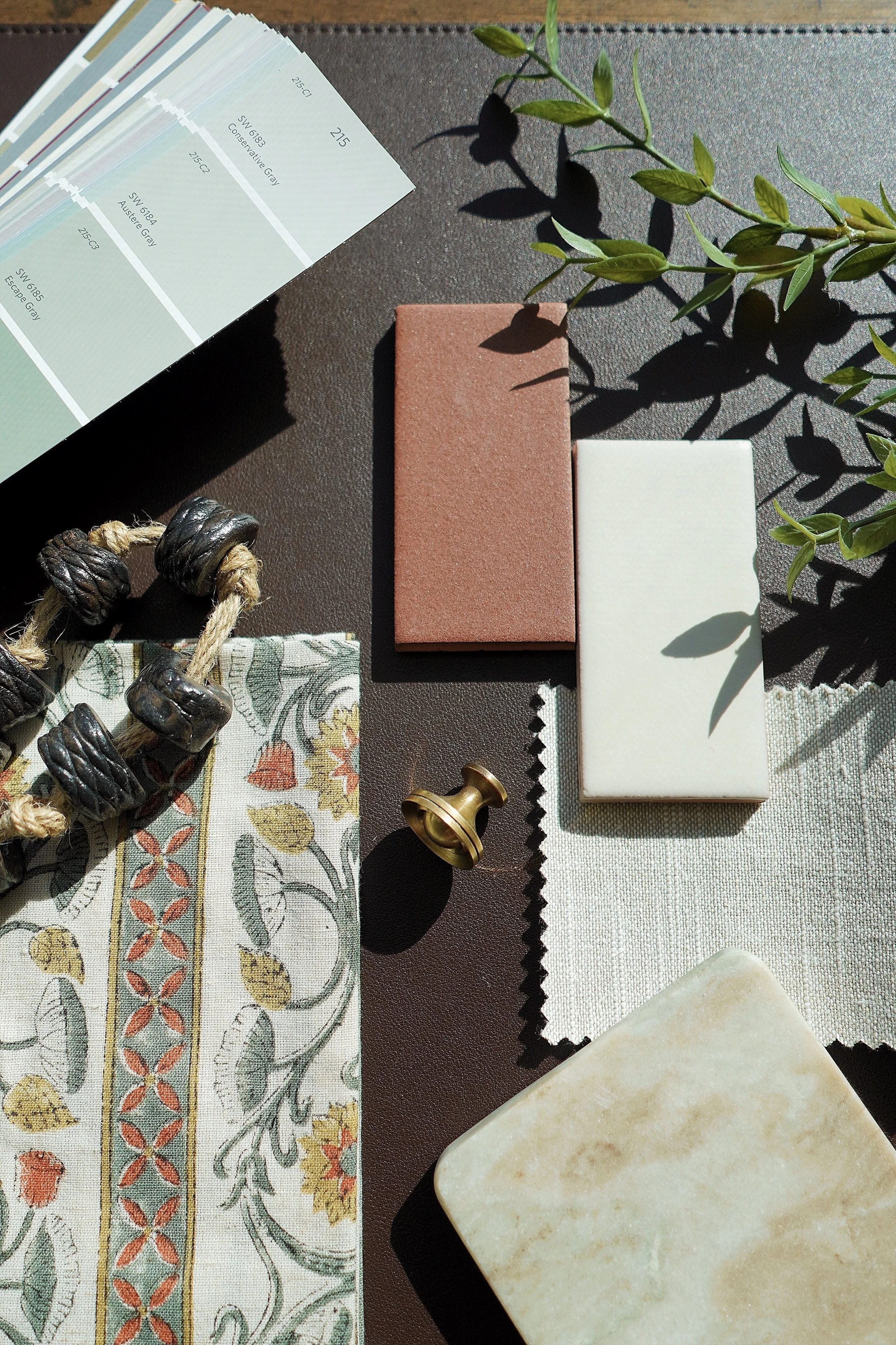 Interior design mood board with paint swatches, fabric samples, tiles, decorative beads, and leaves.