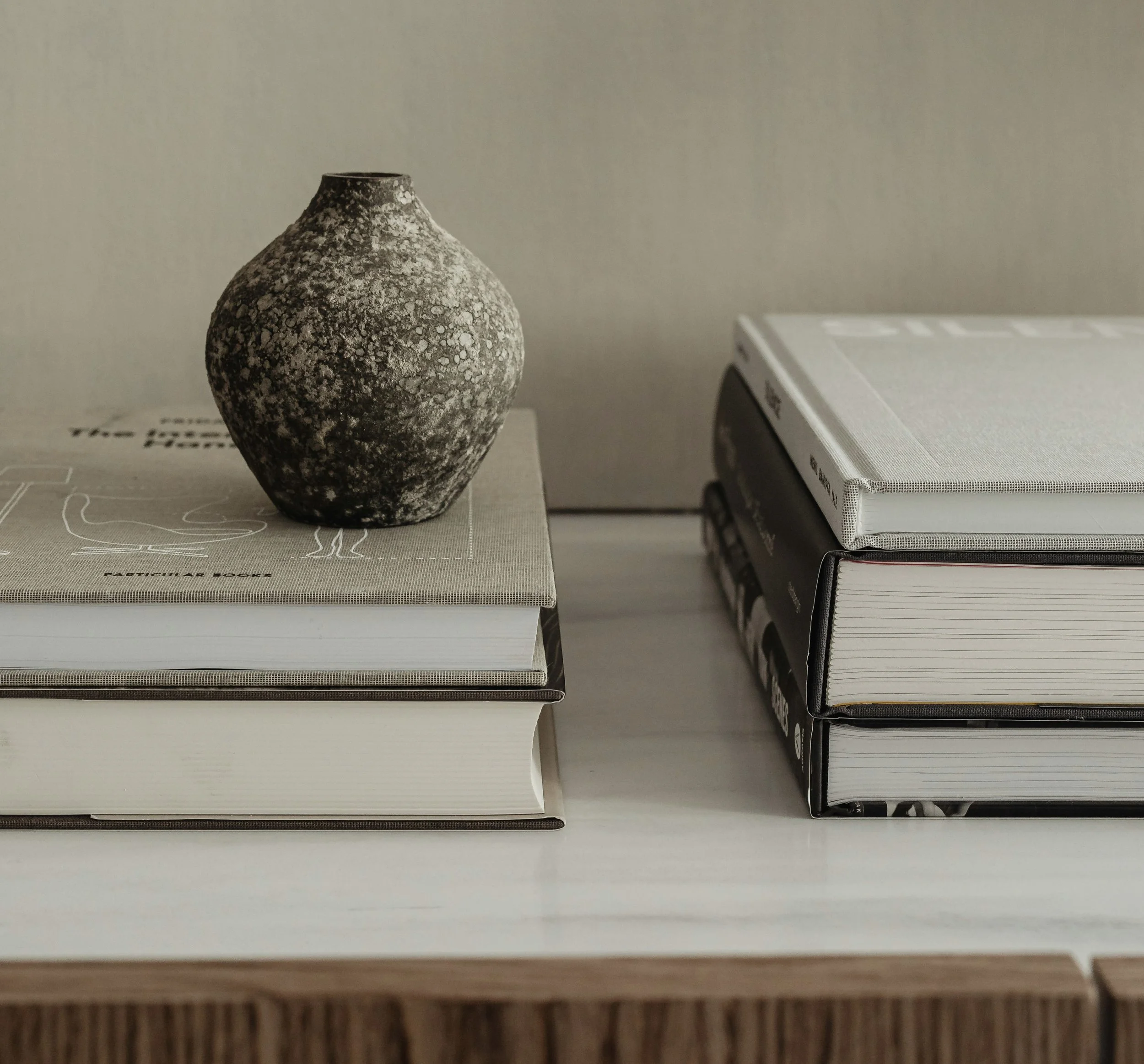 A textured ceramic vase placed on top of a stack of books on a table.