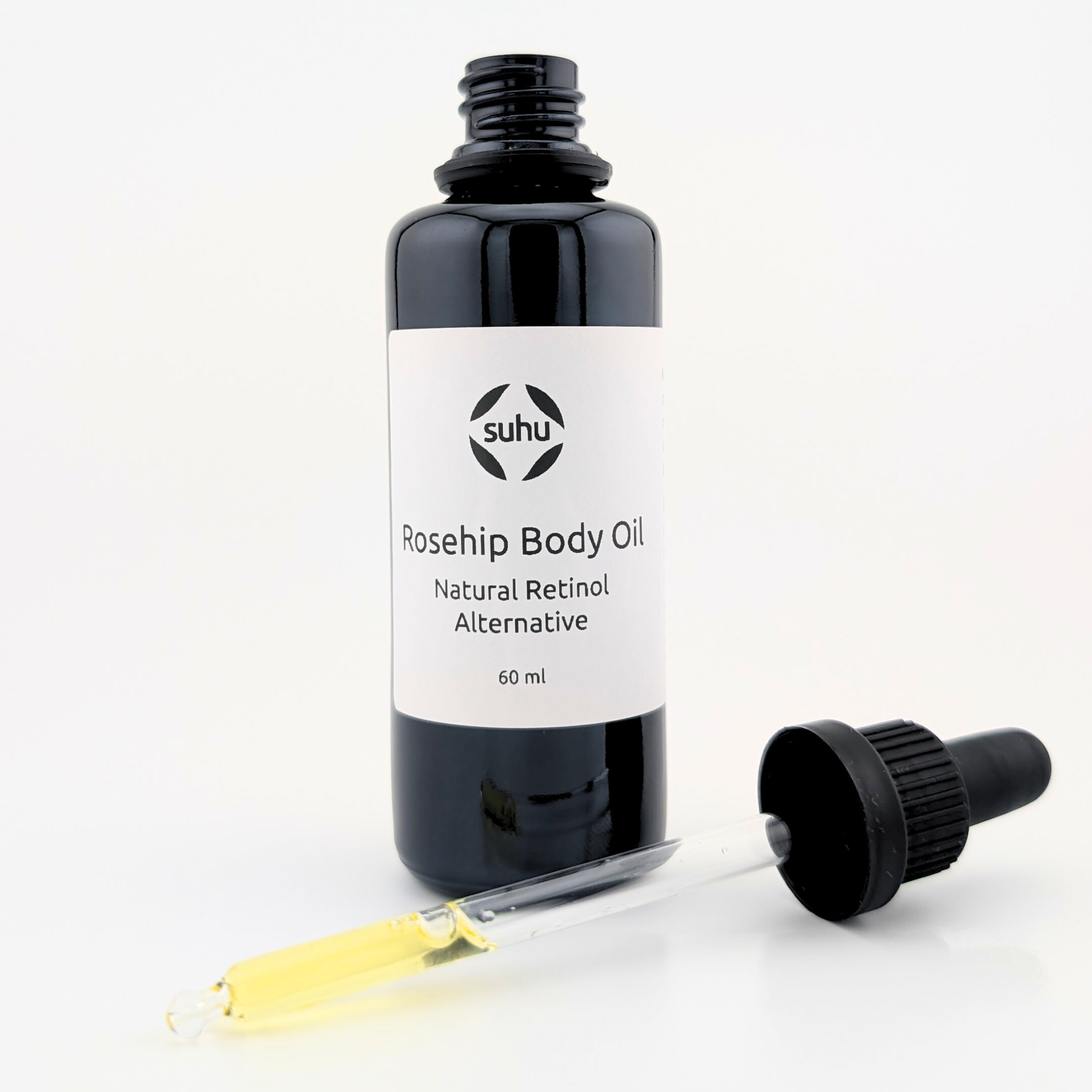 Opened black glass bottle of Rosehip Body Oil with dropper containing golden liquid oil all in front of a white background.