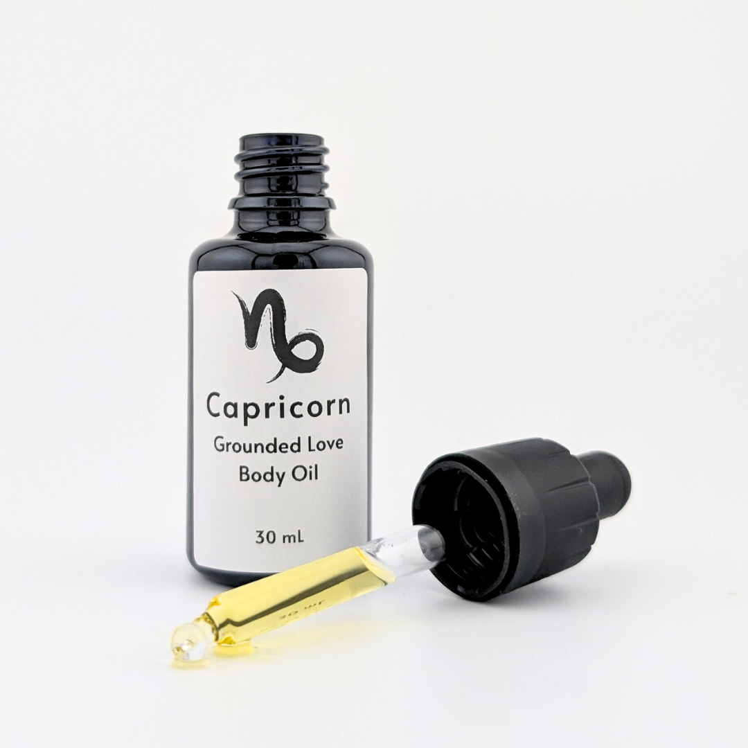 Opened black glass bottle of Capricorn Grounded Love Star Sign body oil with dropper cap showing golden oil material against white background.png