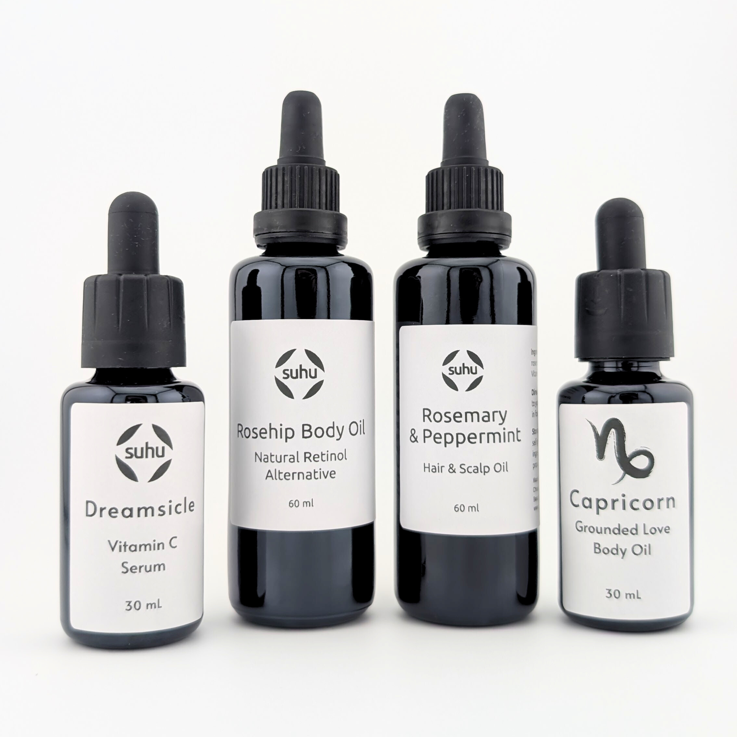 From left to right, bottles of the following products: Vitamin C serum, Rosehip Body Oil, Hair & Scalp Oil, Star Sign Body Oil. Against a white background. Bottles are black with white labels. Labels have black text.