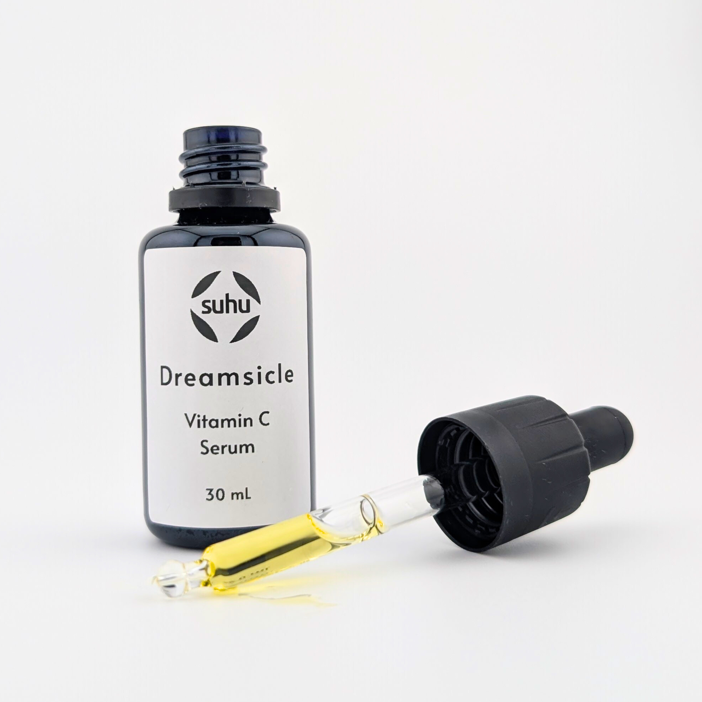 opened black dropper bottle with vitamin c serum label and dropper showing golden oil in front of a white background.