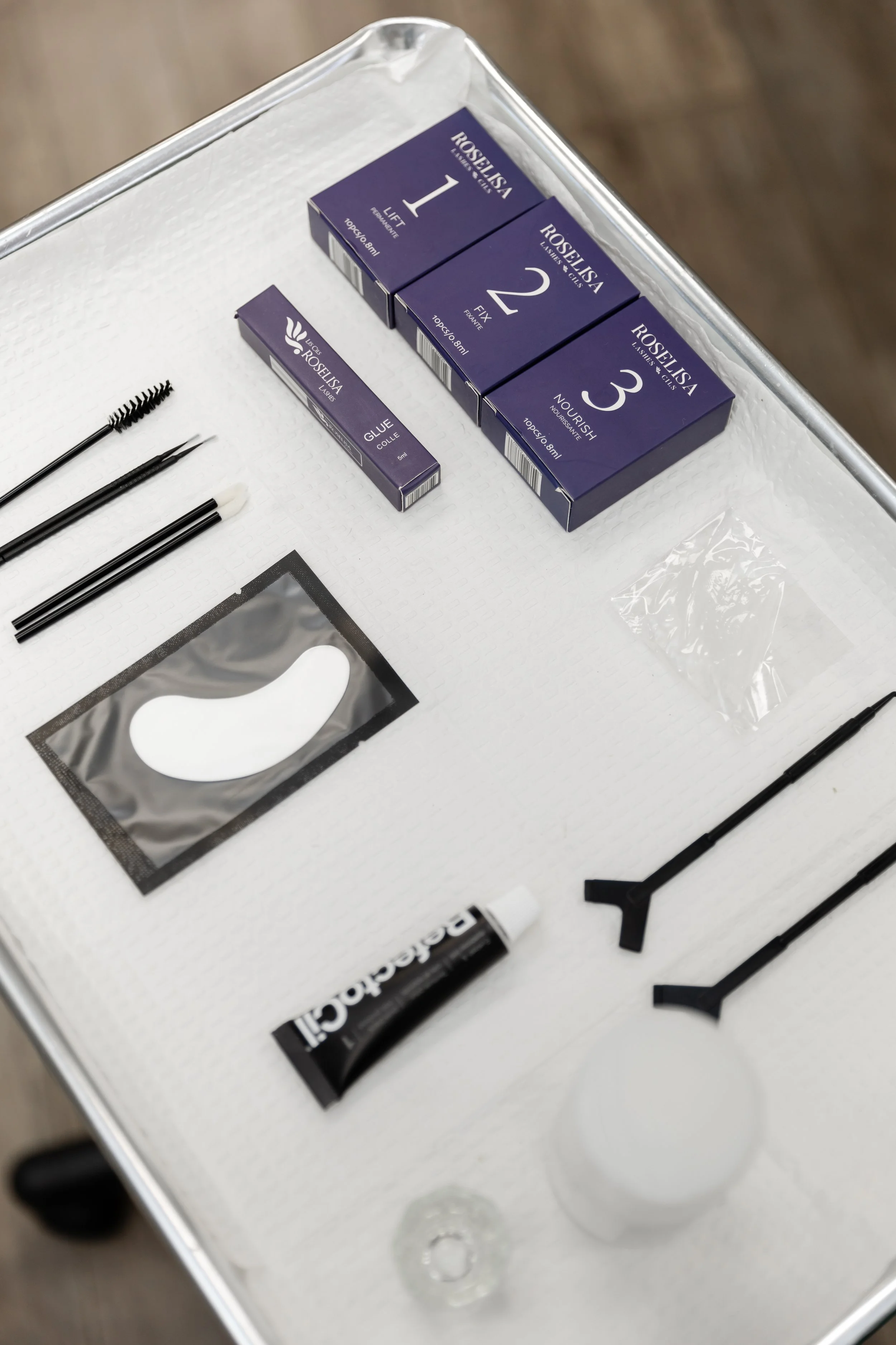 A tray containing eyelash extension tools and supplies, including three boxes labeled with numbers 1, 2, and 3, a glue tube, applicator brushes, and a small package of cotton swabs.