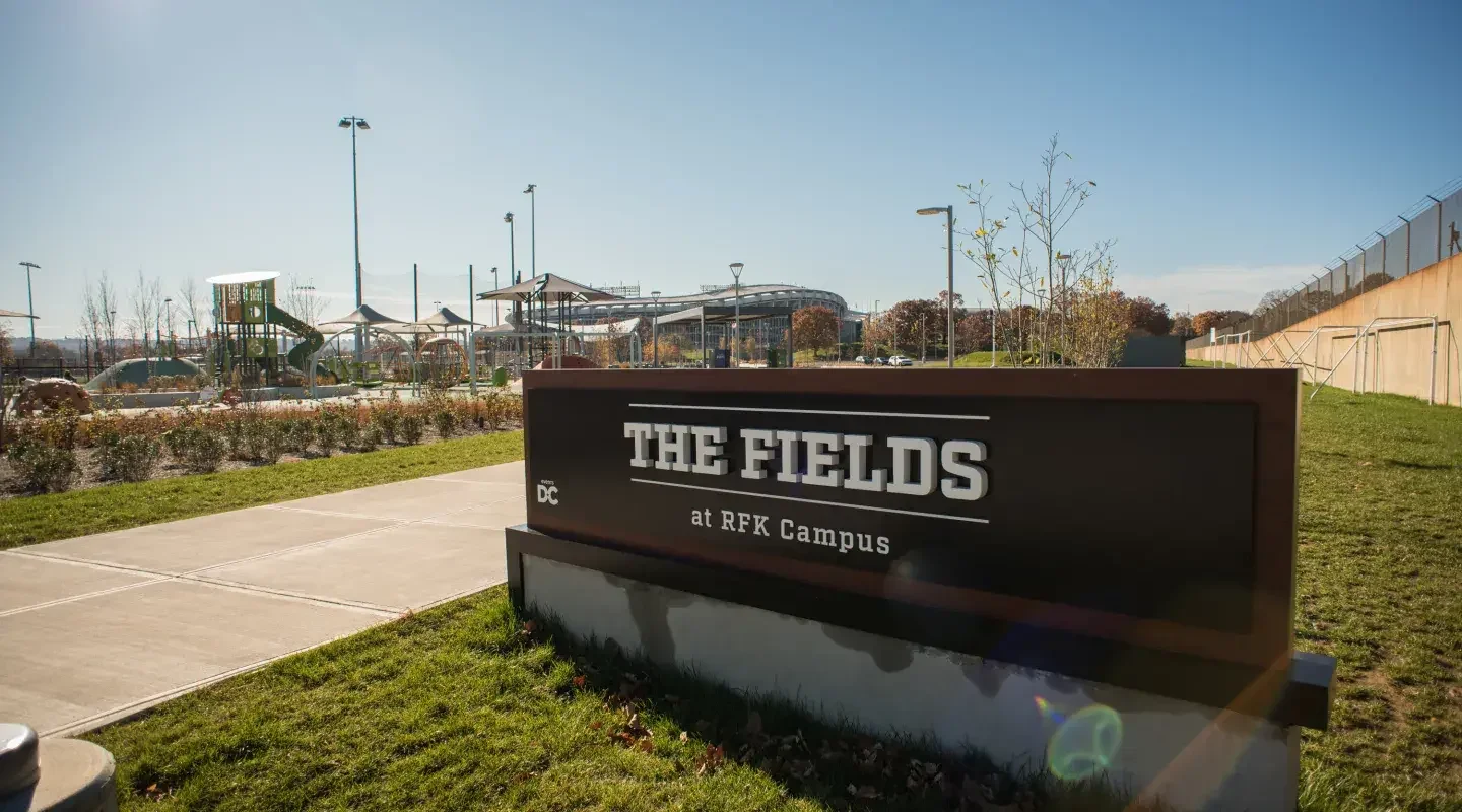 Sign that reads 'The Fields at RFK Campus' with a playground and trees in the background.