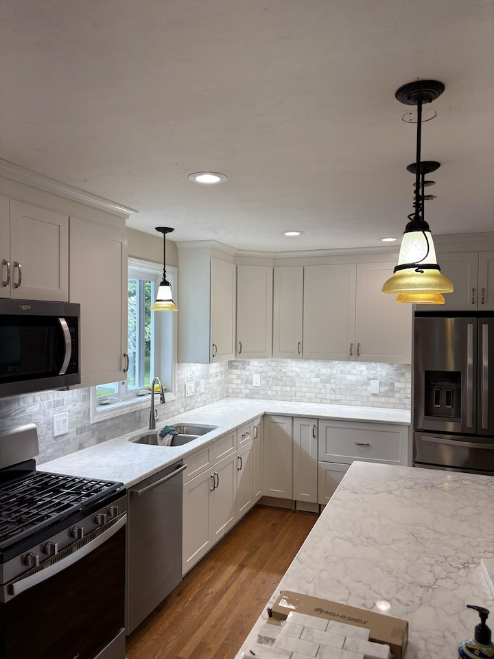 Modern kitchen with white cabinets, marble countertops, stainless steel appliances, and pendant lighting over a breakfast bar, with hardwood floors.
