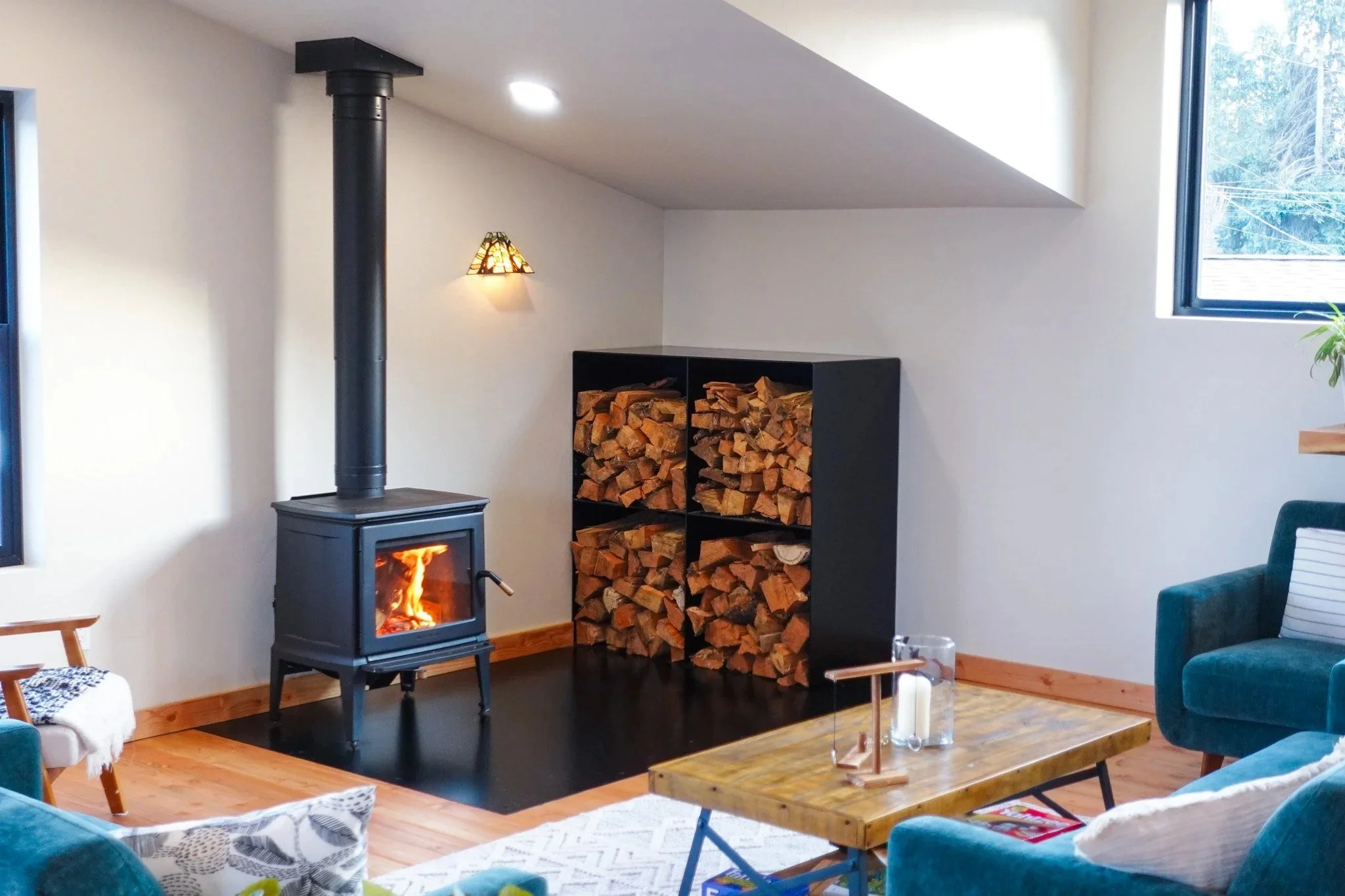Finished wood-stove corner in a Hood River, Oregon home with a custom satin black steel firewood box and a 5x8 flush steel hearth plate, designed and fabricated by de stijl FORMS.