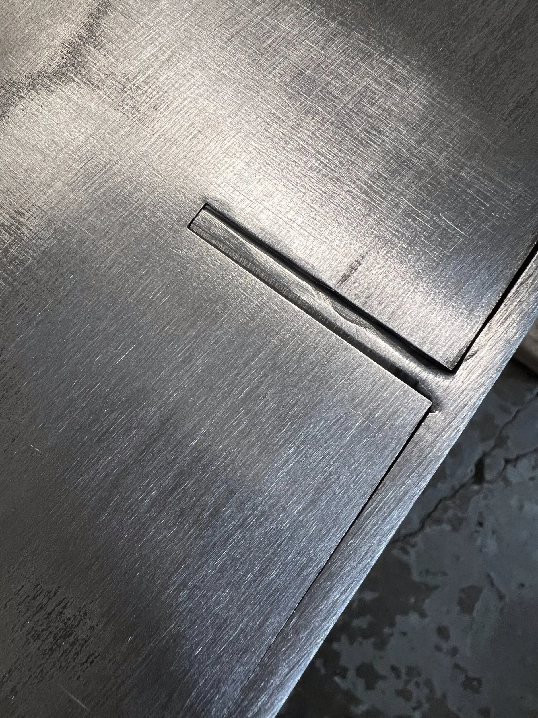 Close-up of the tab-and-slot interlock where the steel back panel meets the top of a custom firewood box — designed and fabricated by de stijl FORMS in Hood River, Oregon.