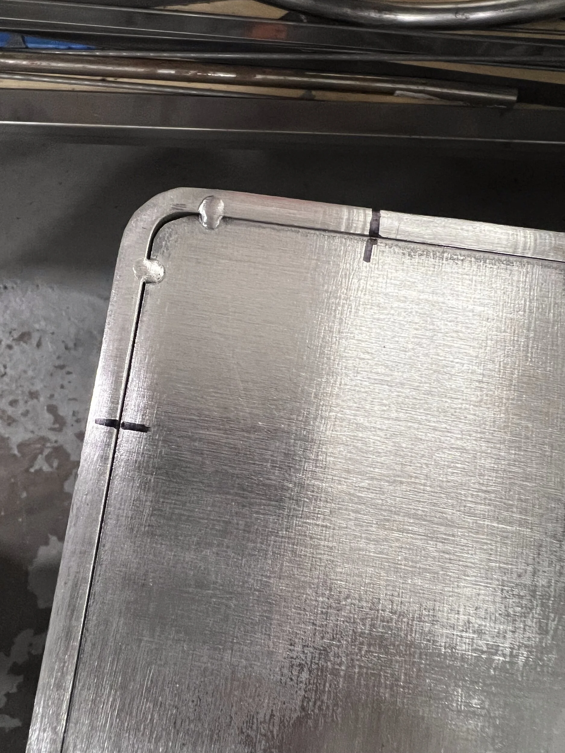 Corner of a steel firewood box back panel showing tab-and-slot connections plug welded through the slots — designed and fabricated by de stijl FORMS in Hood River, Oregon.