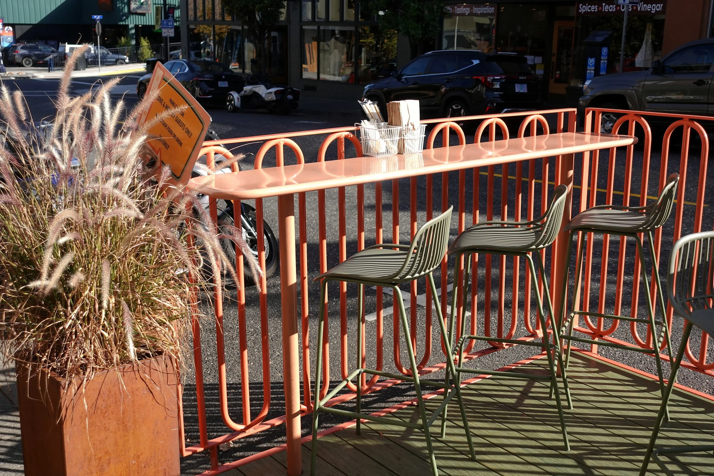 Custom steel railing and integrated seating area at the Love & Hominy parklet, combining the coral steelwork and green decking into a cohesive extension of the restaurant.