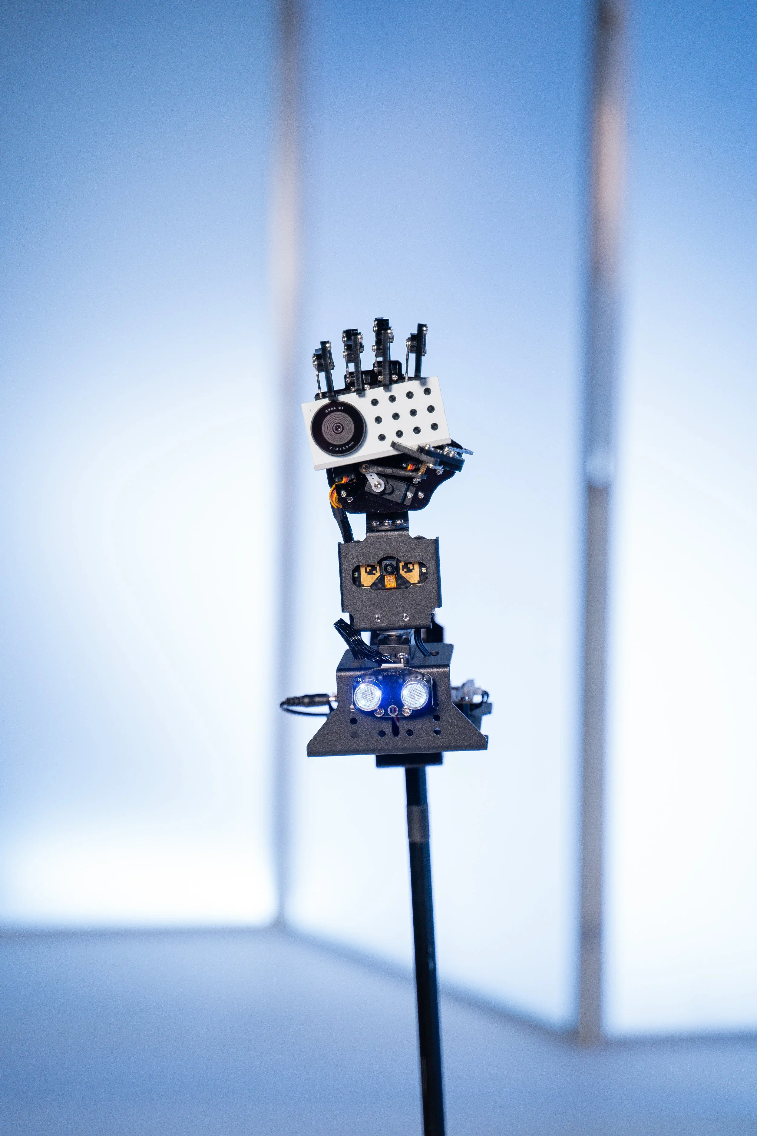 A robotic hand with sensors and mechanical components, attached to a stand, in a minimalistic setting featuring aluminum set back drops designed and fabricated by de stijl FORMS