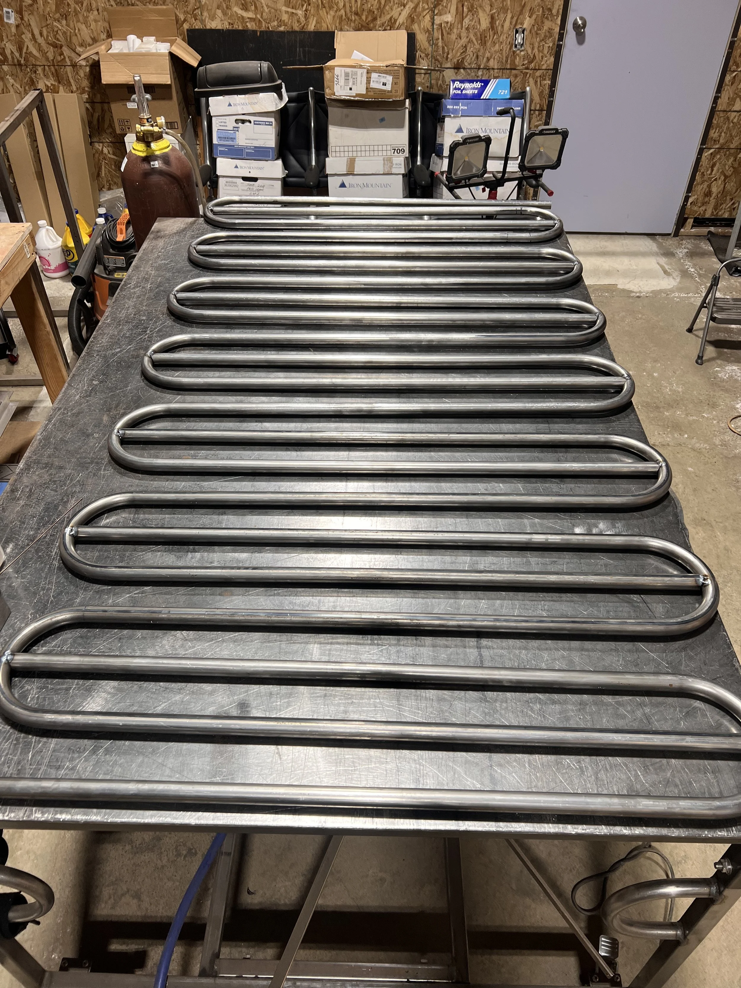 Hand-bent steel railing components arranged during fabrication for the Love & Hominy parklet, showing the repeated geometry before final assembly and TIG welding.