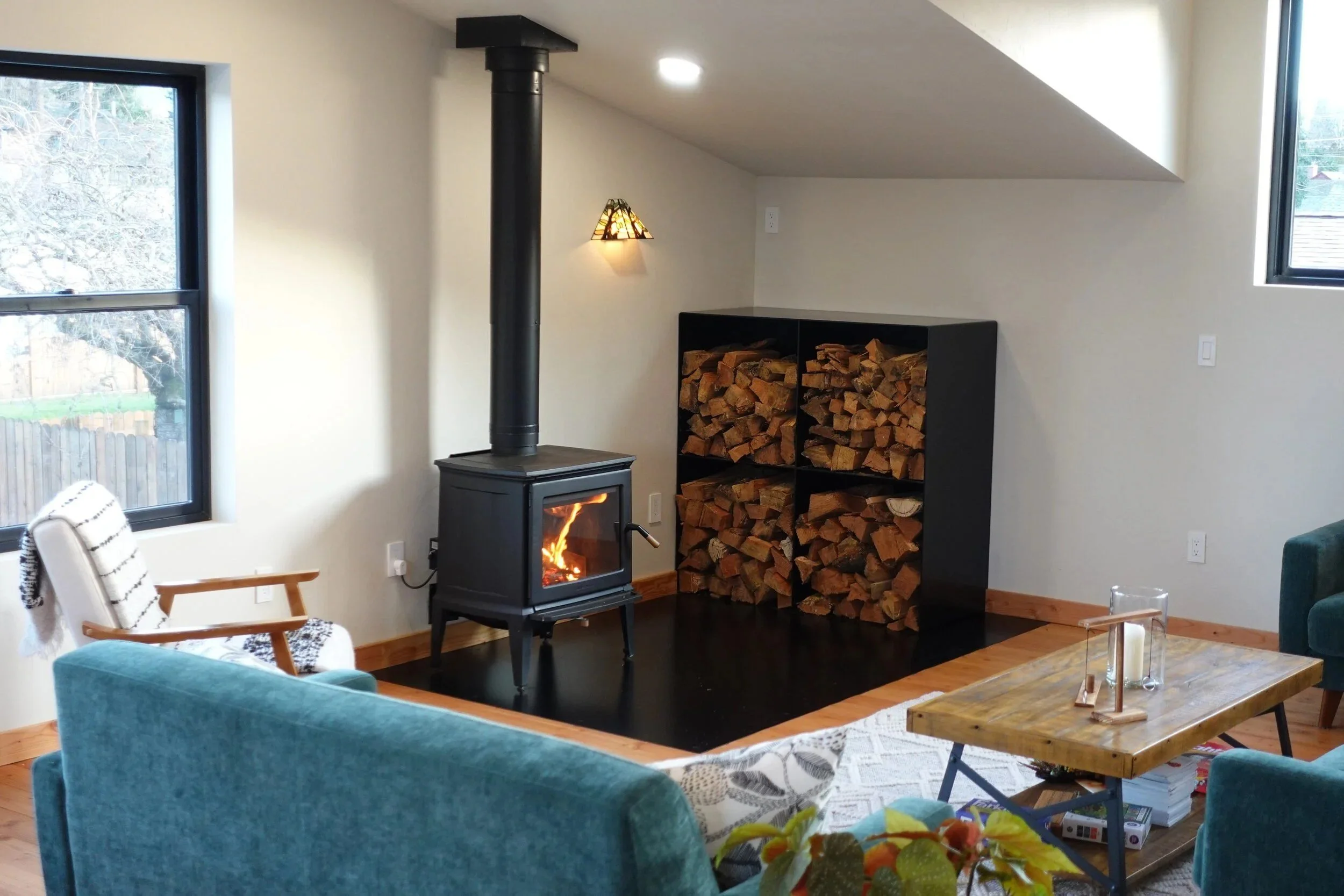 Finished living room with a wood stove, satin black steel firewood box, and flush steel hearth — designed and fabricated by de stijl FORMS in Hood River, Oregon.