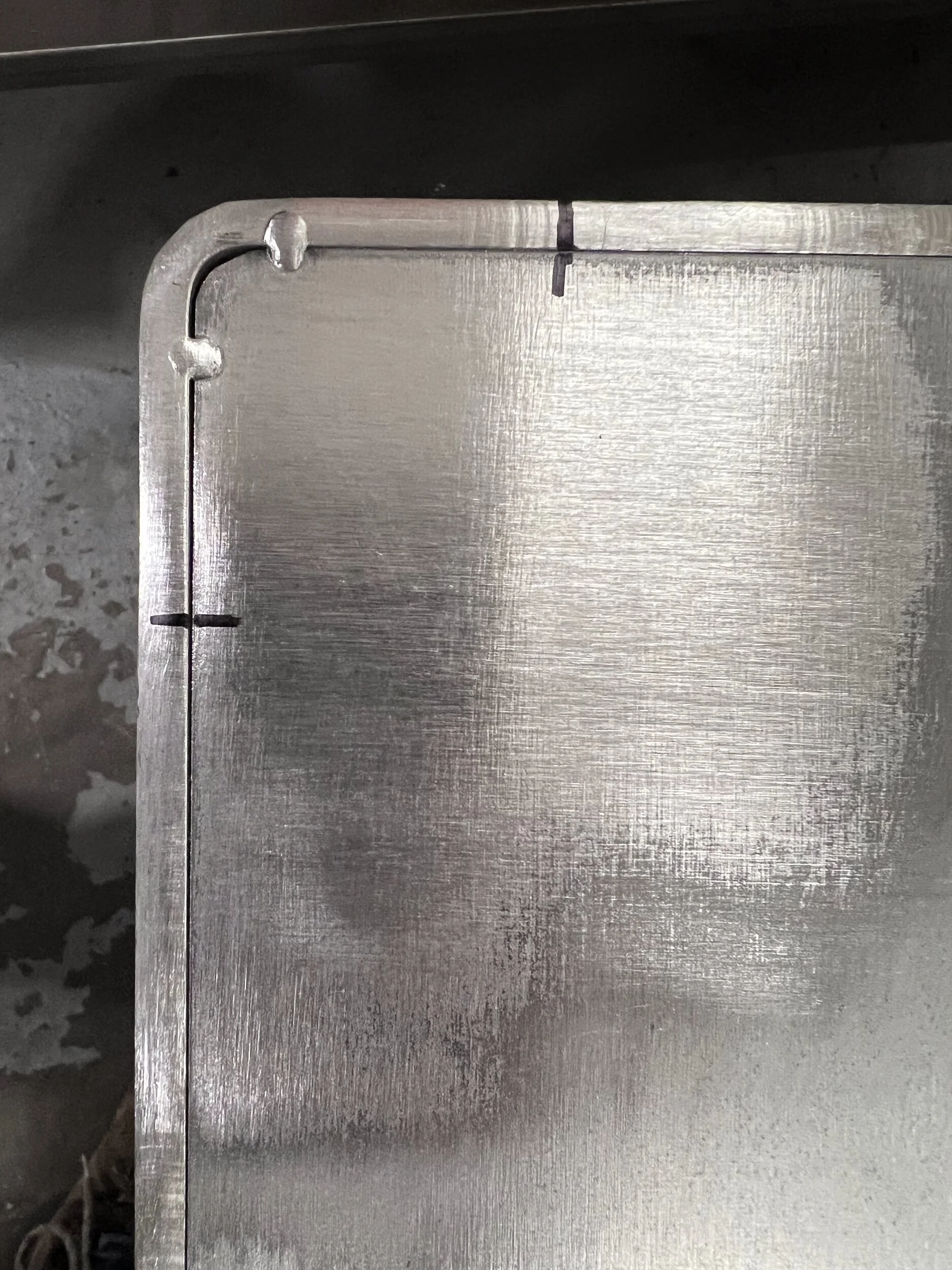 Tab-and-slot corner joints on a steel firewood box back panel, plug welded and ground smooth before finishing — designed and fabricated by de stijl FORMS in Hood River, Oregon.