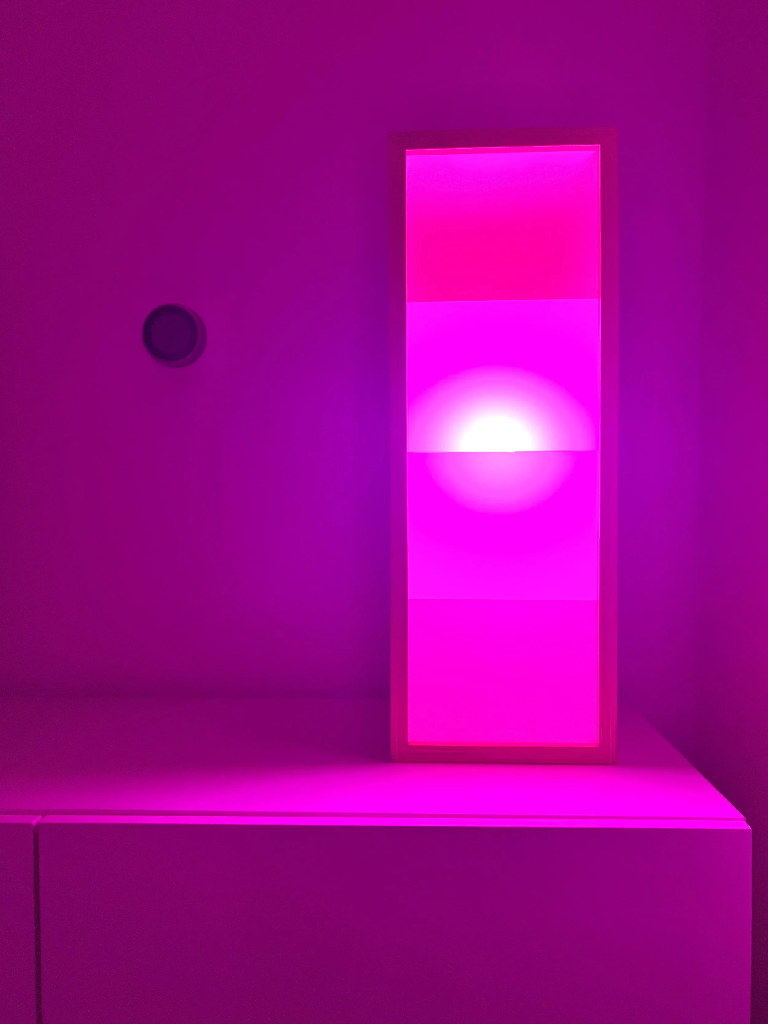 Pink illuminated rectangular light fixture on a white surface, with pink and purple lighting effects