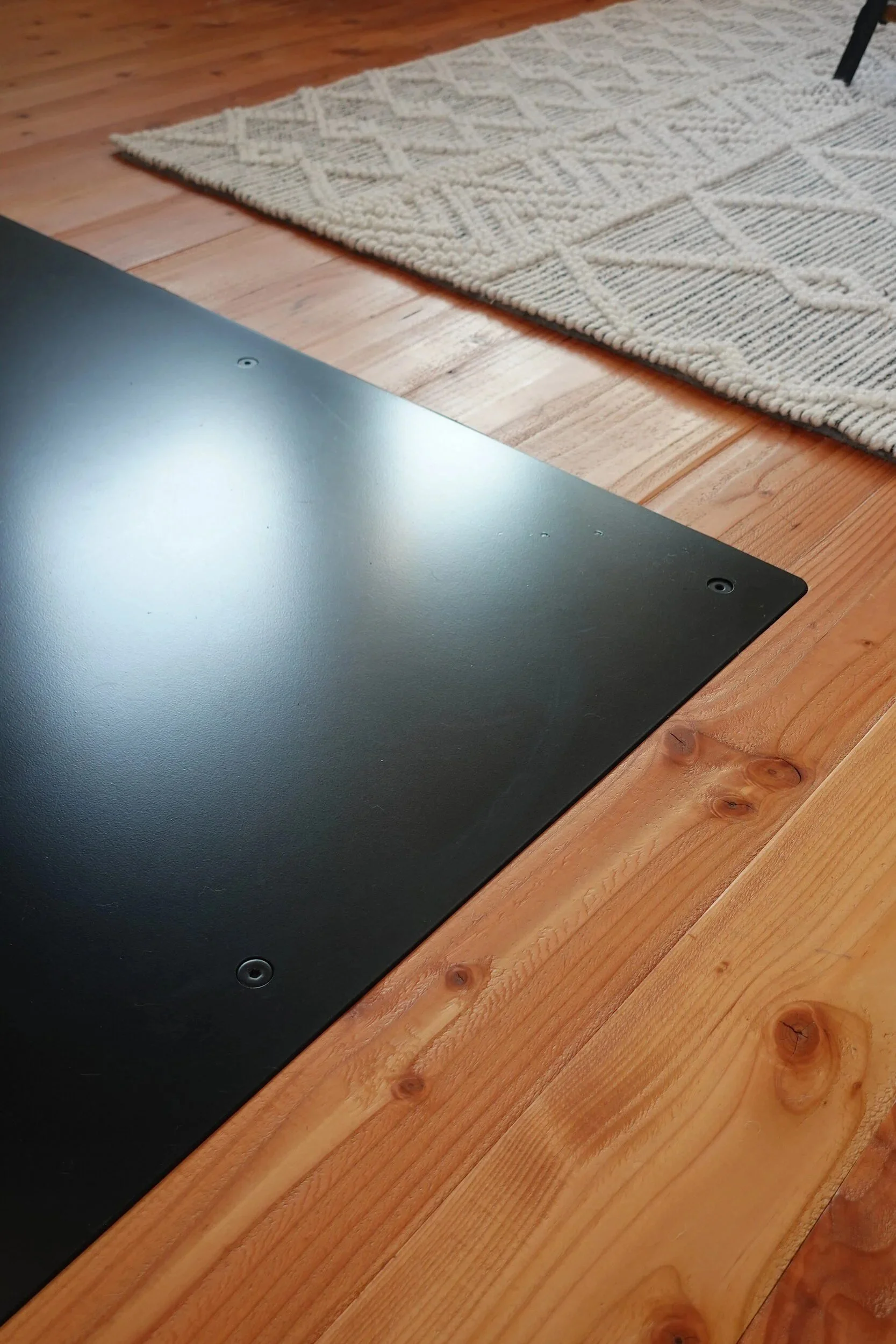 Satin black steel hearth plate meeting a patterned rug and wood floor in a finished living space — designed and fabricated by de stijl FORMS in Hood River, Oregon.