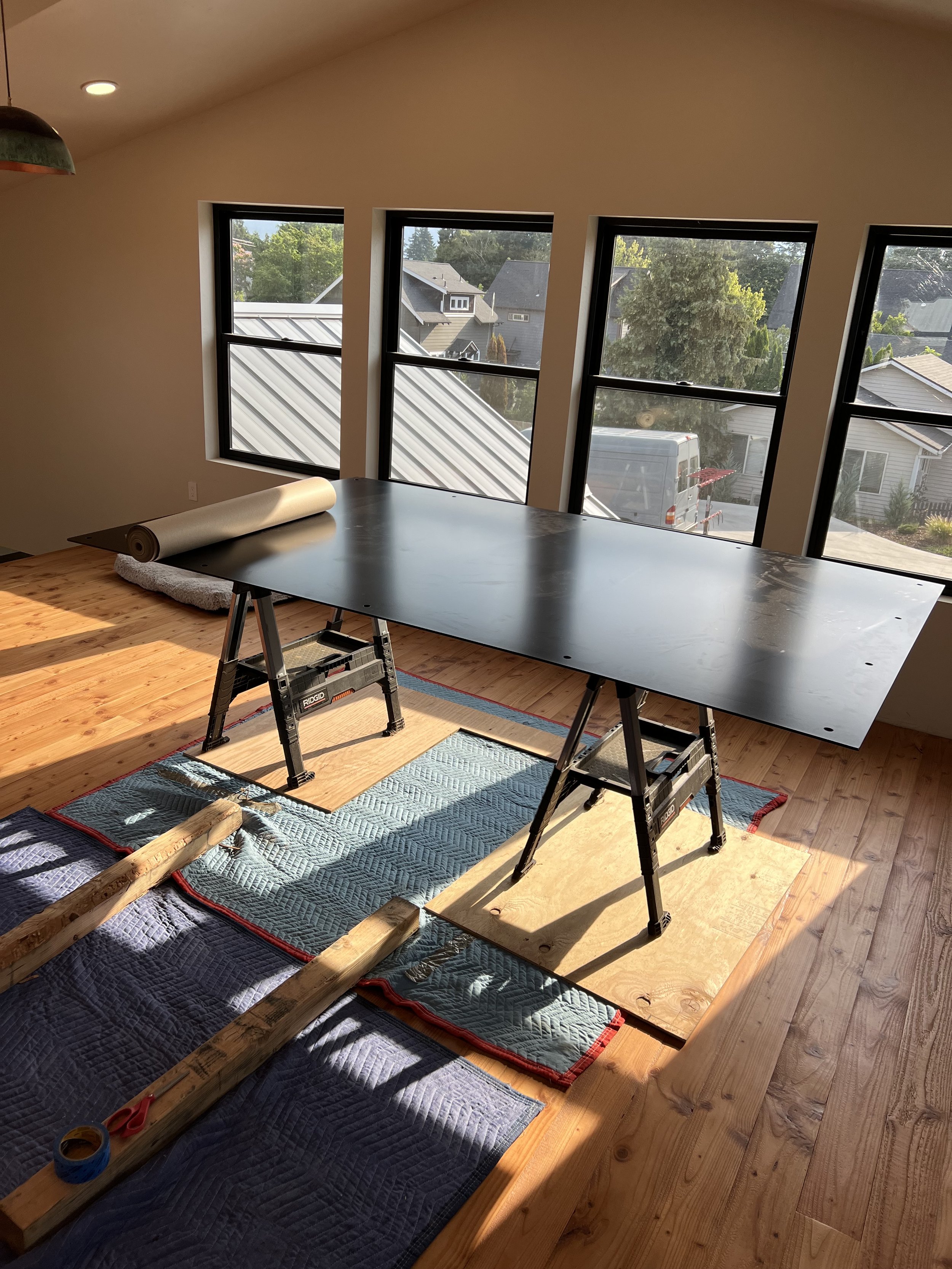 5x8 black steel hearth plate test-fit on sawhorses in the sunlit second-floor room before being recessed into the floor — designed and fabricated by de stijl FORMS in Hood River, Oregon.