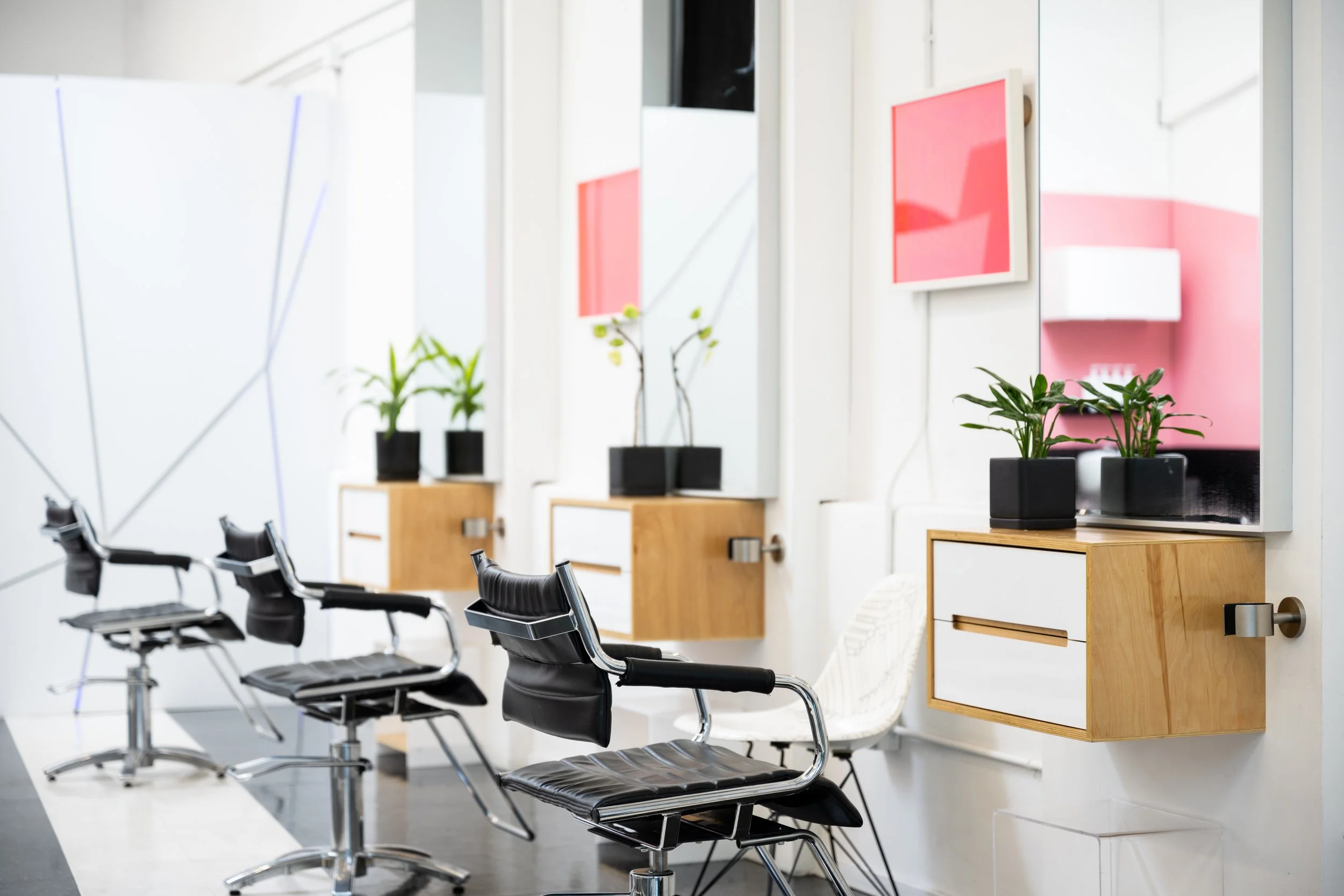 Interior of a modern salon with black chairs, mirrors, potted plants, and colorful pink artwork on the wall.