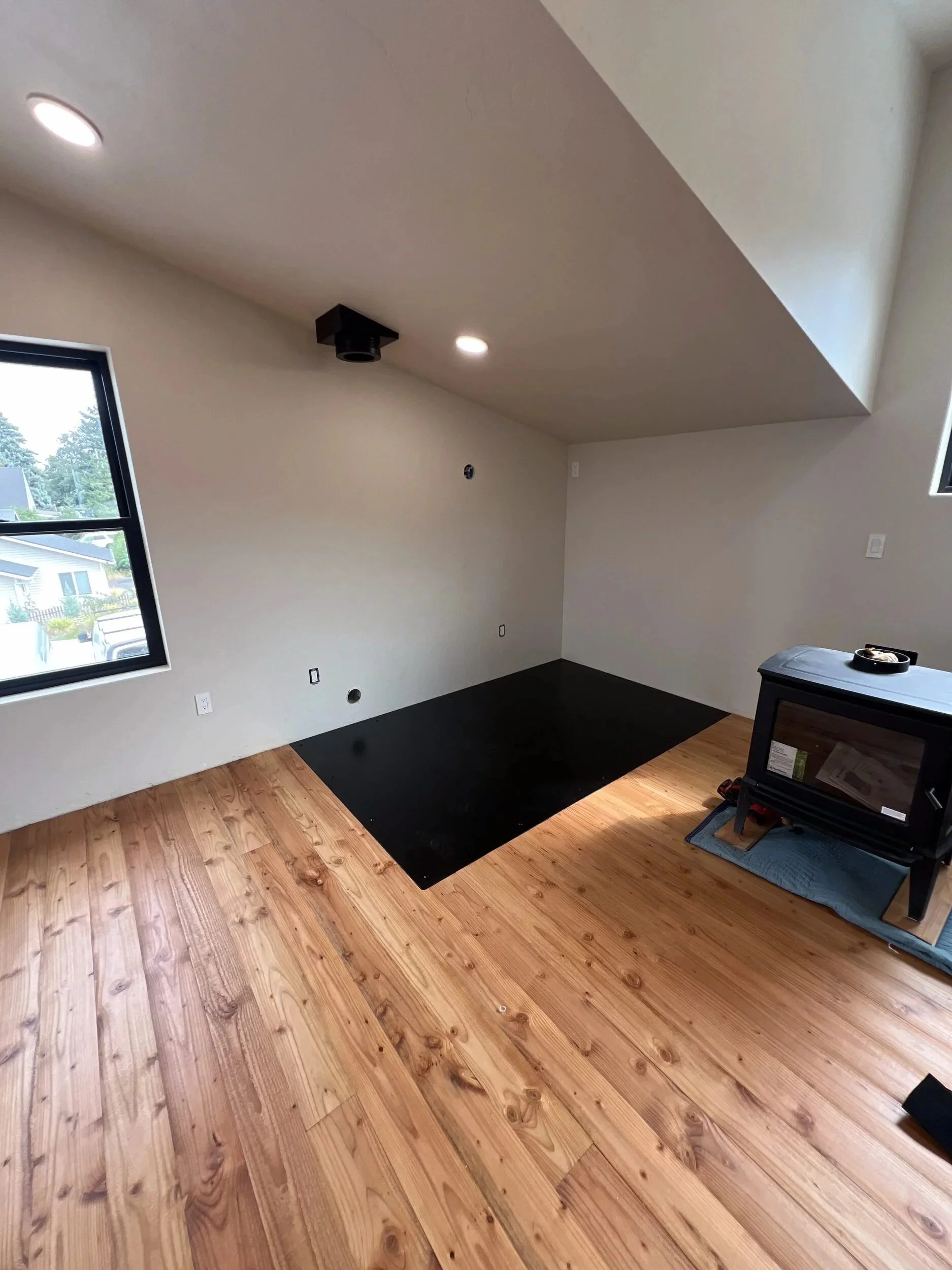 Steel firewood box set in place on the flush hearth plate in a bright, newly finished room — designed and fabricated by de stijl FORMS in Hood River, Oregon.