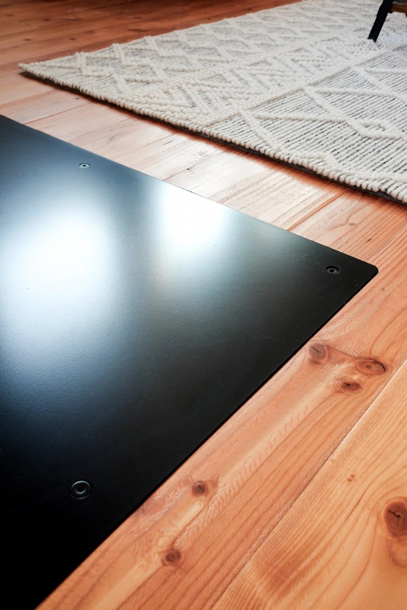 Close-up of a black steel hearth plate set flush with a fir wood floor, showing the clean transition between steel and wood — designed and fabricated by de stijl FORMS in Hood River, Oregon.