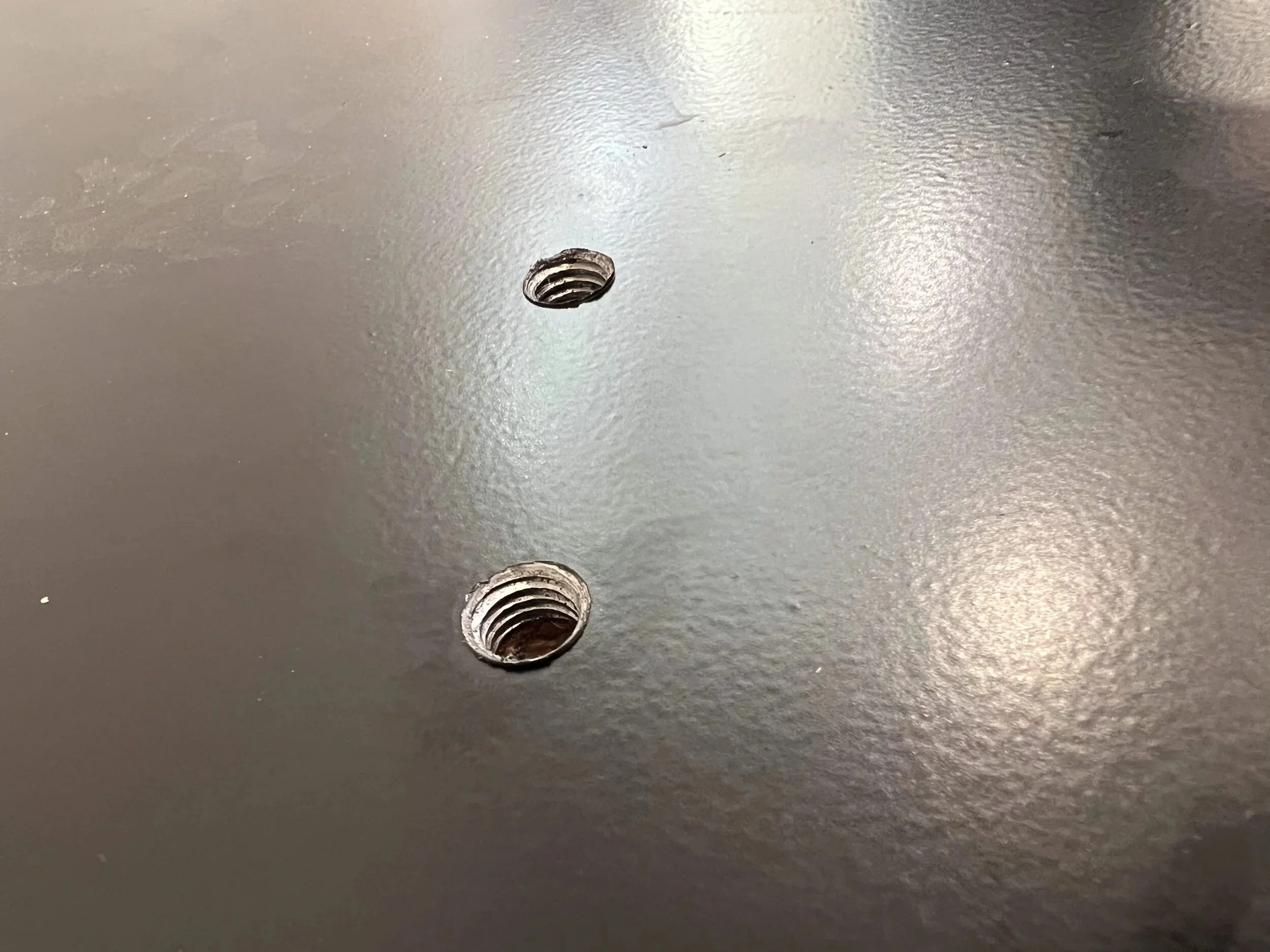 Threaded inserts set into a steel hearth plate to receive bolts from the firewood box above — designed and fabricated by de stijl FORMS in Hood River, Oregon.