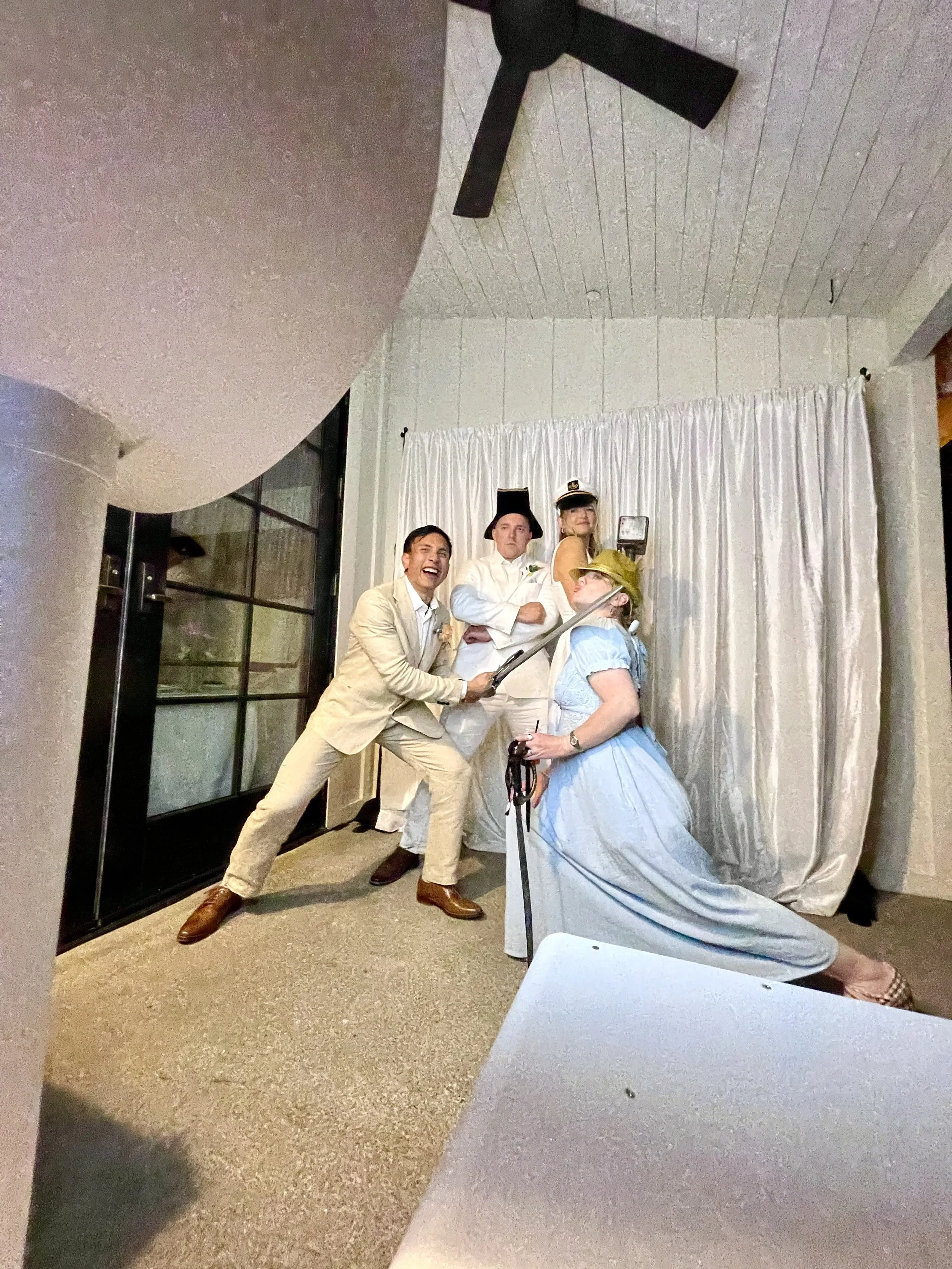 Wedding guests dressed in playful costumes posing with props in front of a white photo booth backdrop