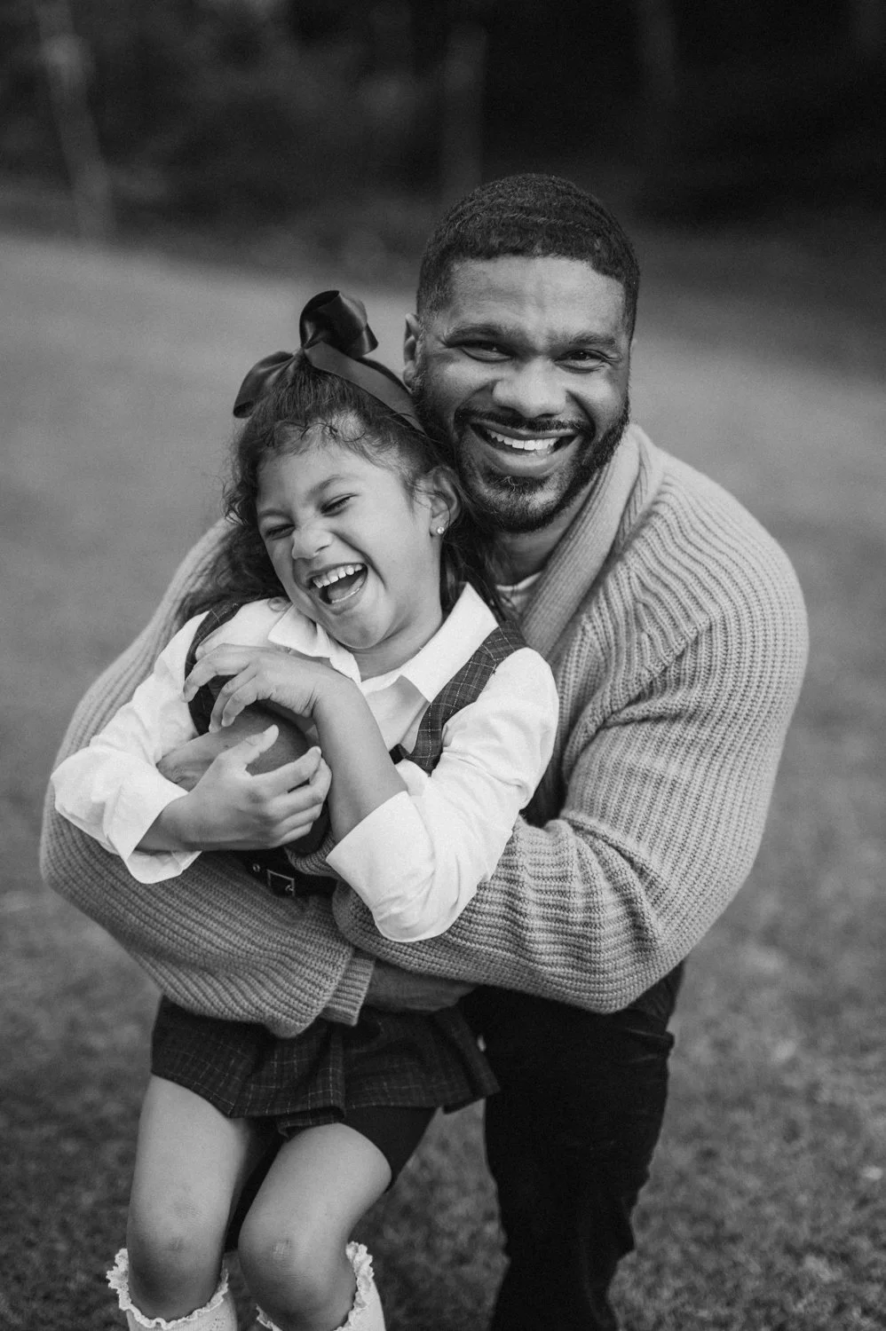 A man and young girl laughing and hugging outdoors, black and white photo.