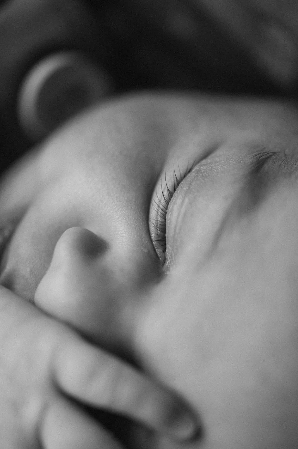 Close-up of a person's face with eyes closed, in black and white, showing eyelashes, eyelid, and part of the nose.