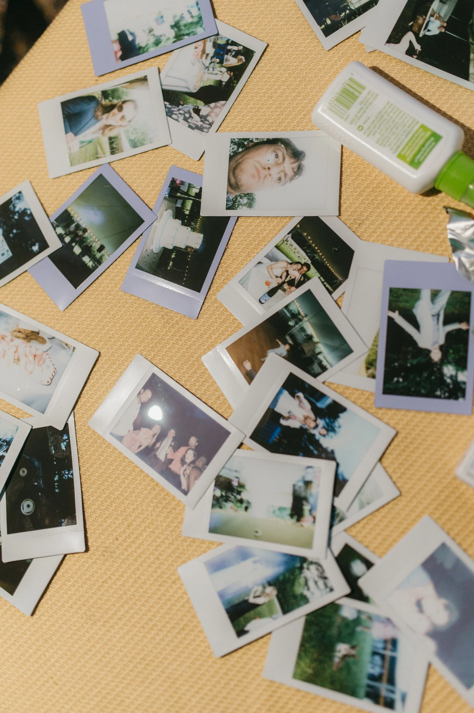Scattered instant photographs on a textured table, featuring people, outdoor scenes, and a birthday cake.