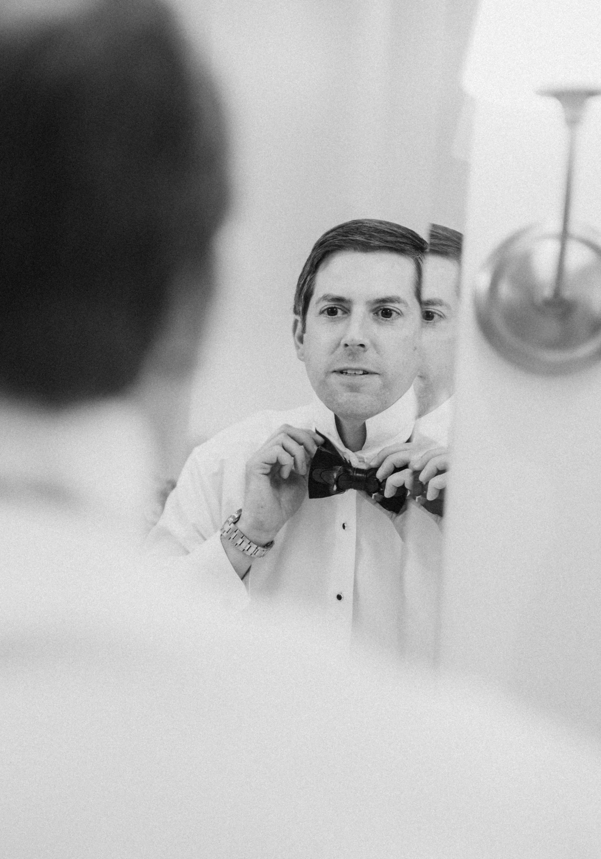 Man adjusting his bowtie while looking in the mirror, black and white photo