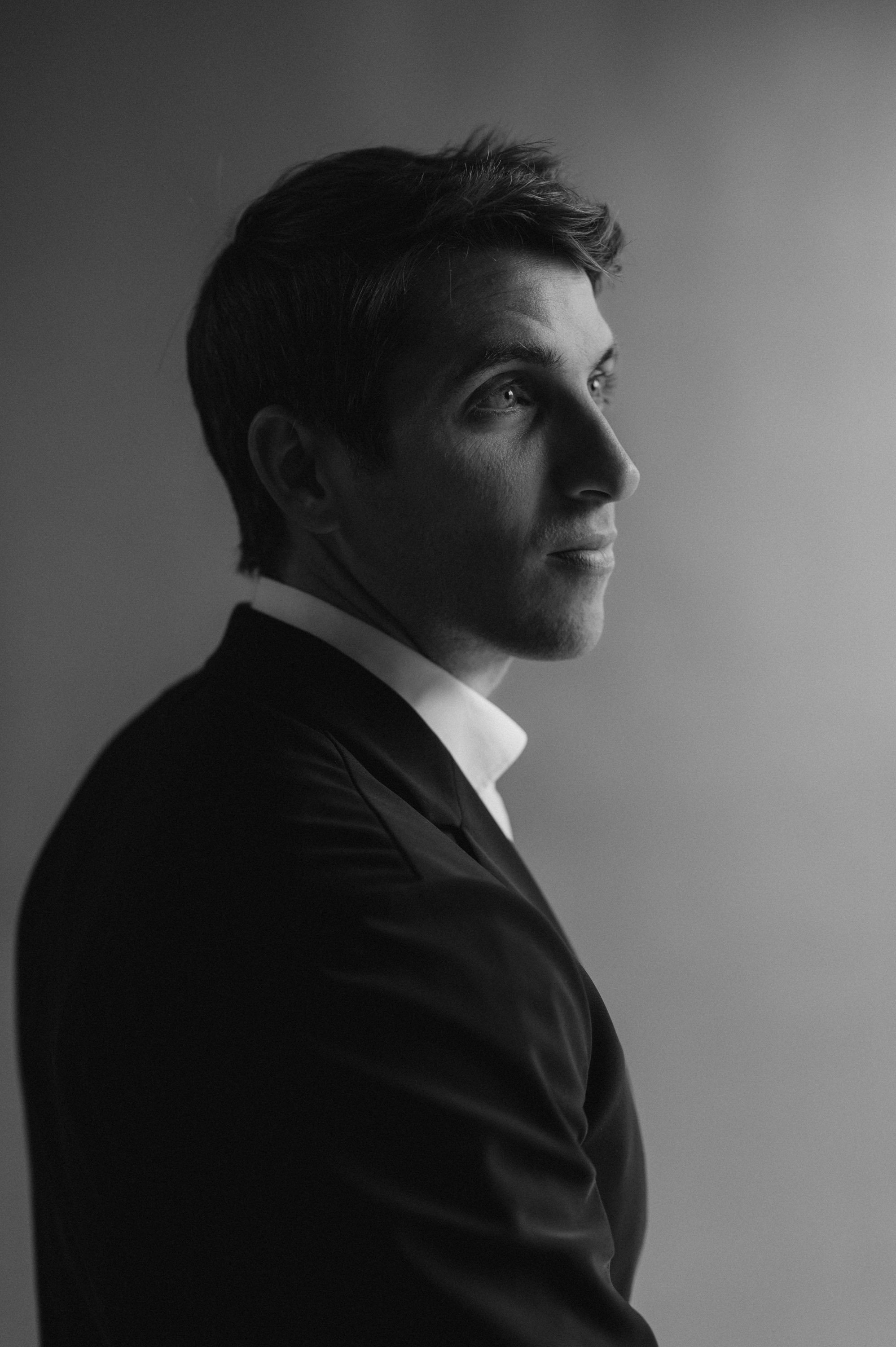 Black and white portrait of a young man in a suit, looking to the right, against a plain background.
