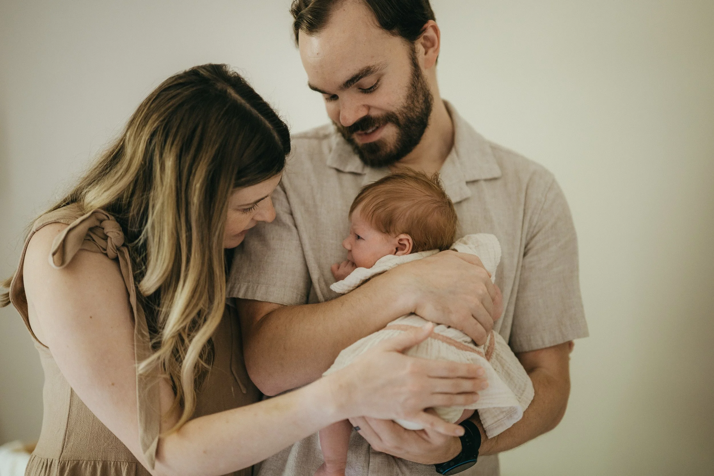 A family of three, including a mother, father, and baby, sharing a tender moment together indoors.
