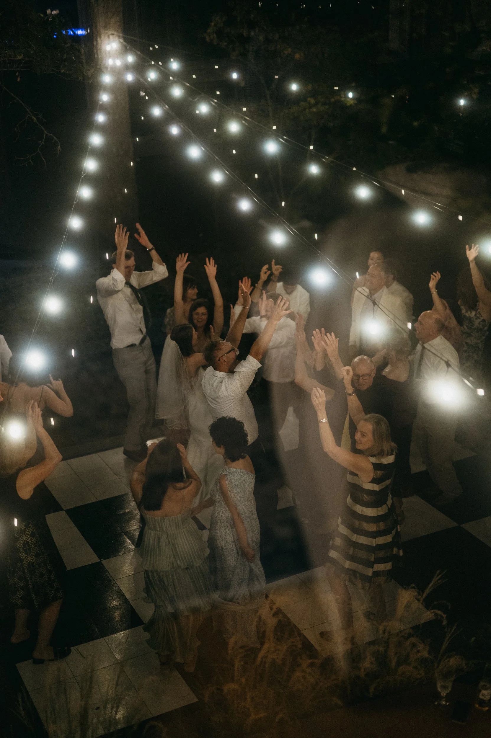 People dancing and celebrating under string lights at a nighttime outdoor event