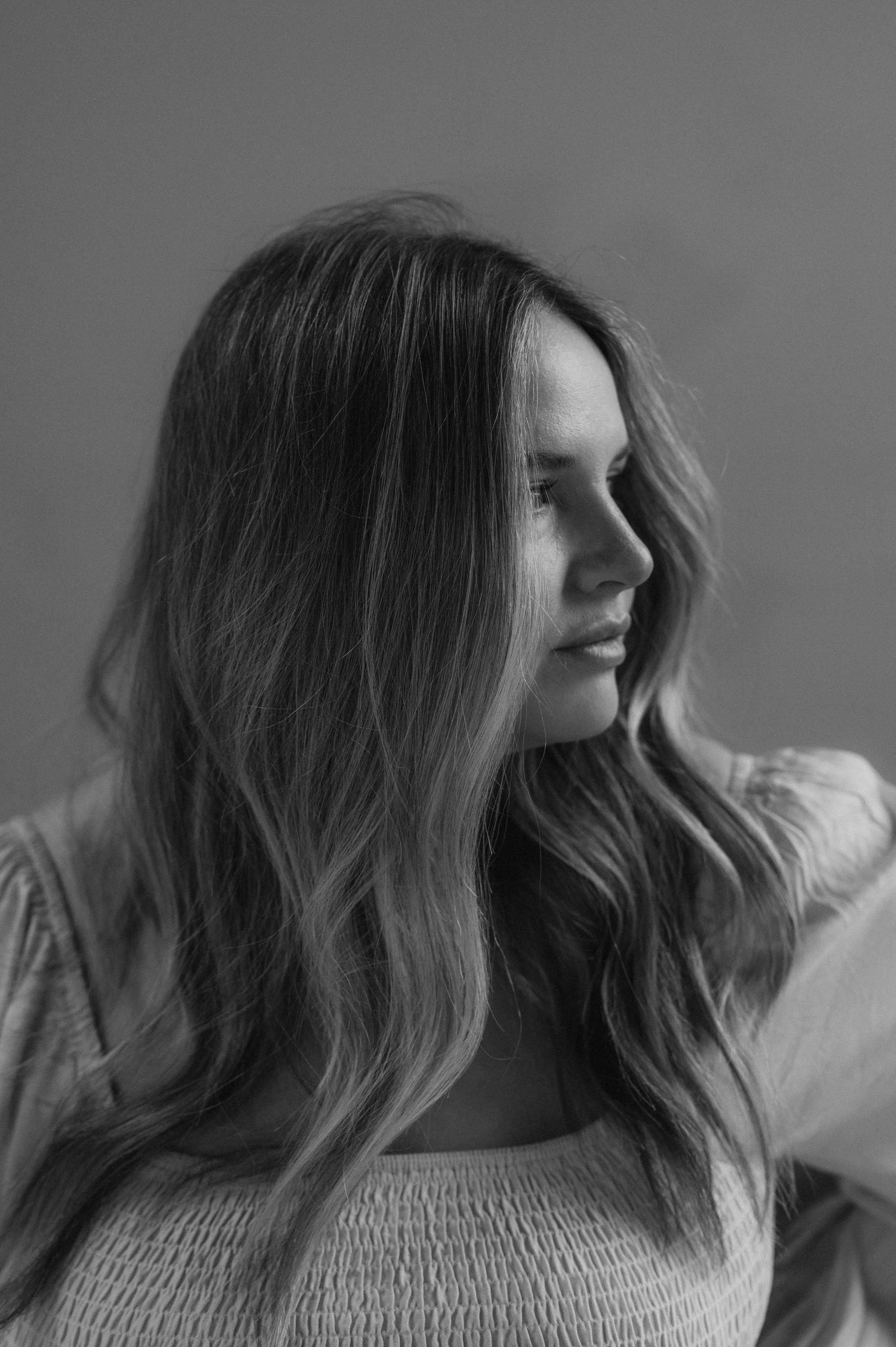 Black and white photo of a young woman with wavy hair looking to the side, wearing a textured top.