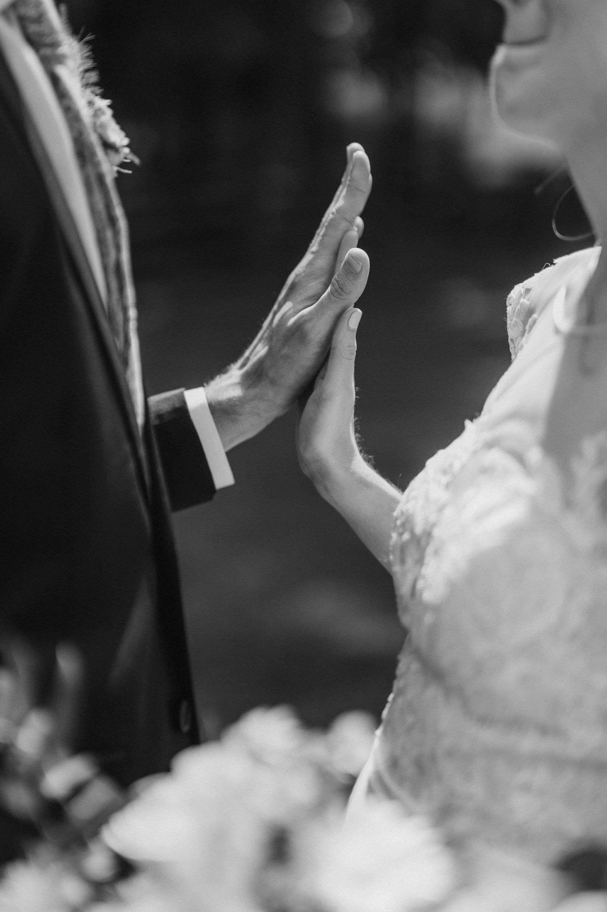 A bride and groom touching hands during a wedding ceremony, black and white photograph.