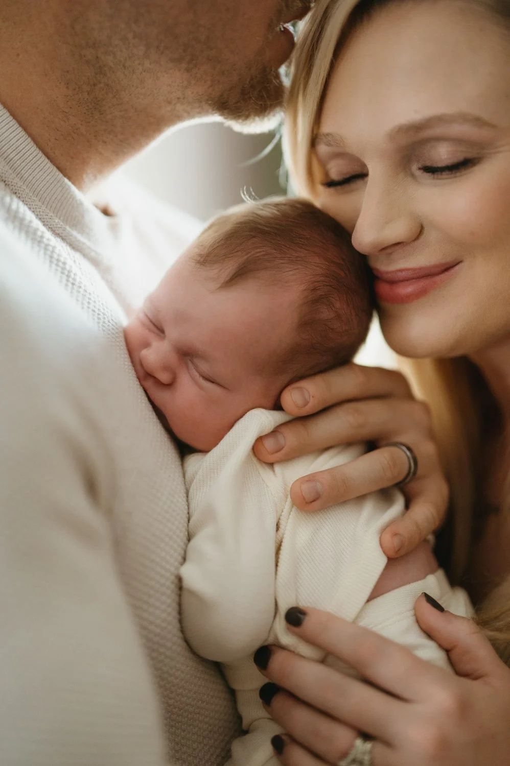 A couple holding their newborn baby close to their faces, smiling affectionately together.
