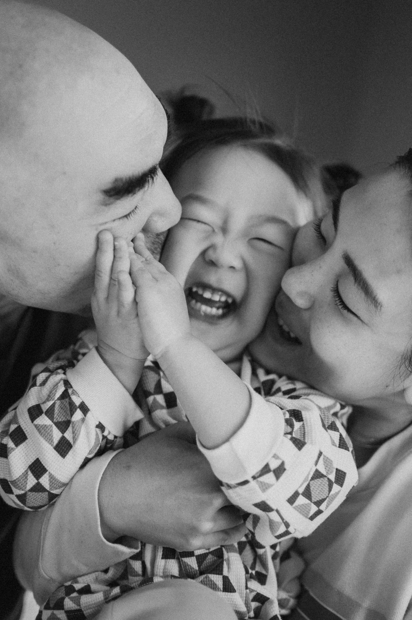 A happy family of three, a father, mother, and child, sharing a joyful moment together. The child is smiling broadly, and the parents are engaging with the child affectionately.
