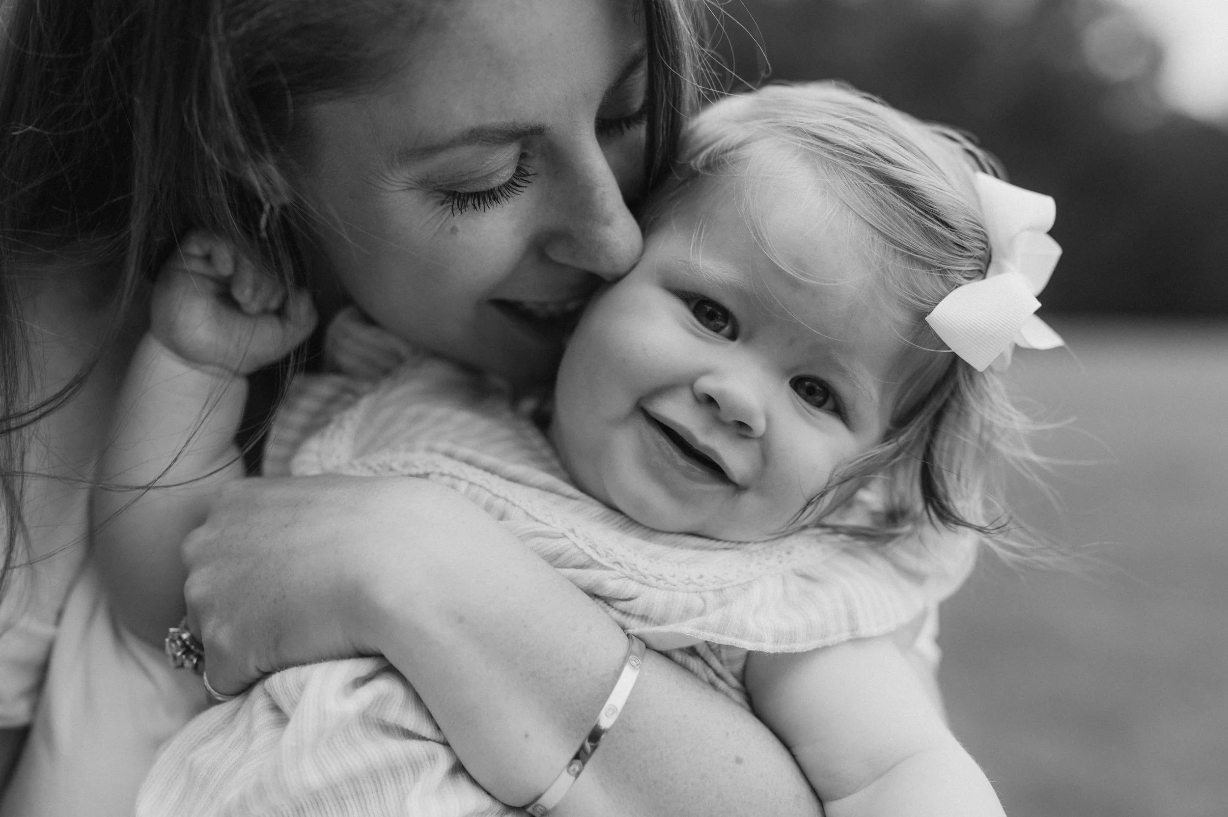 A woman holding a smiling young girl with a bow in her hair.