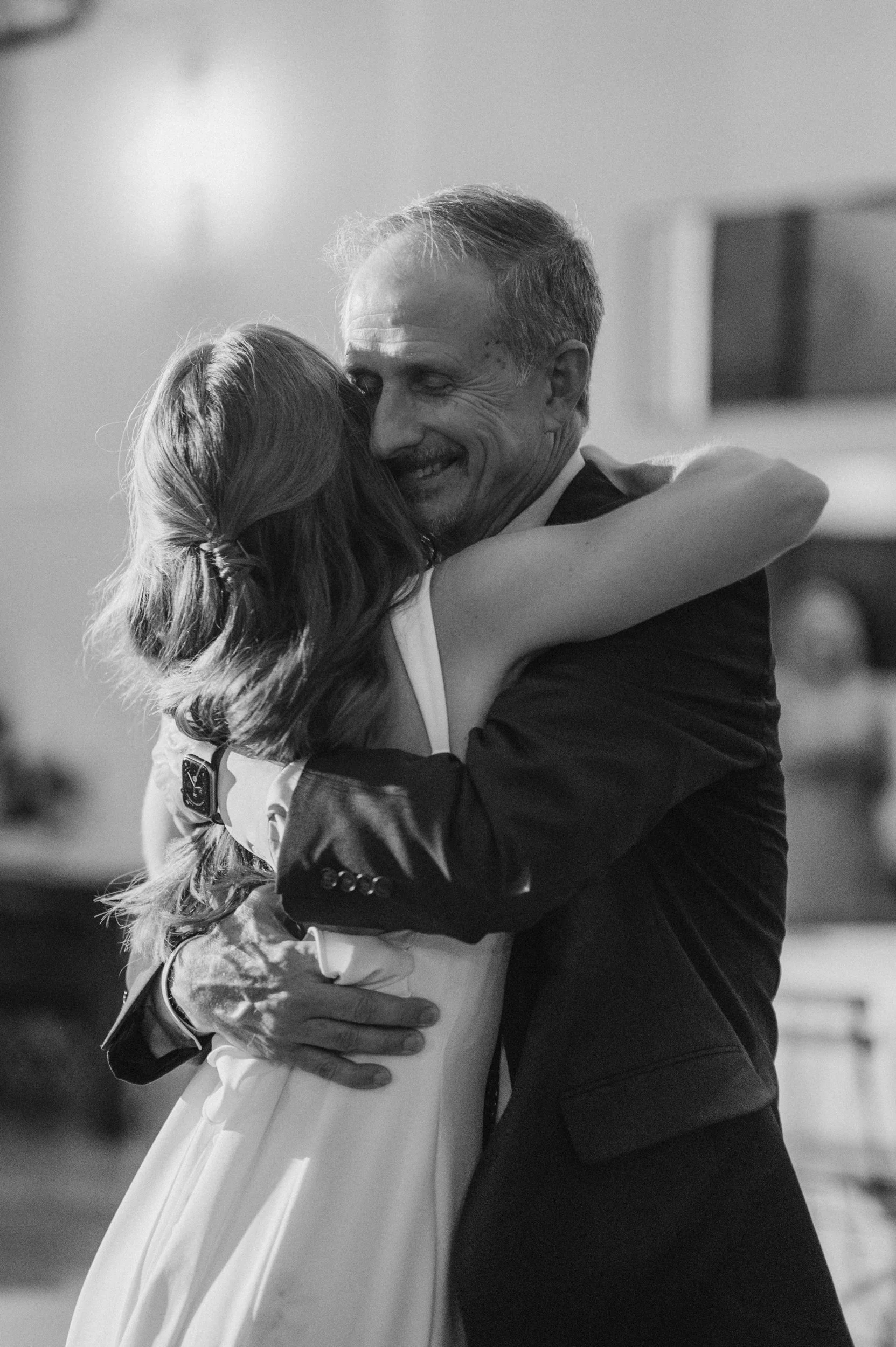 A black and white photo of a man and a woman hugging each other closely, smiling, at what appears to be a celebratory event.