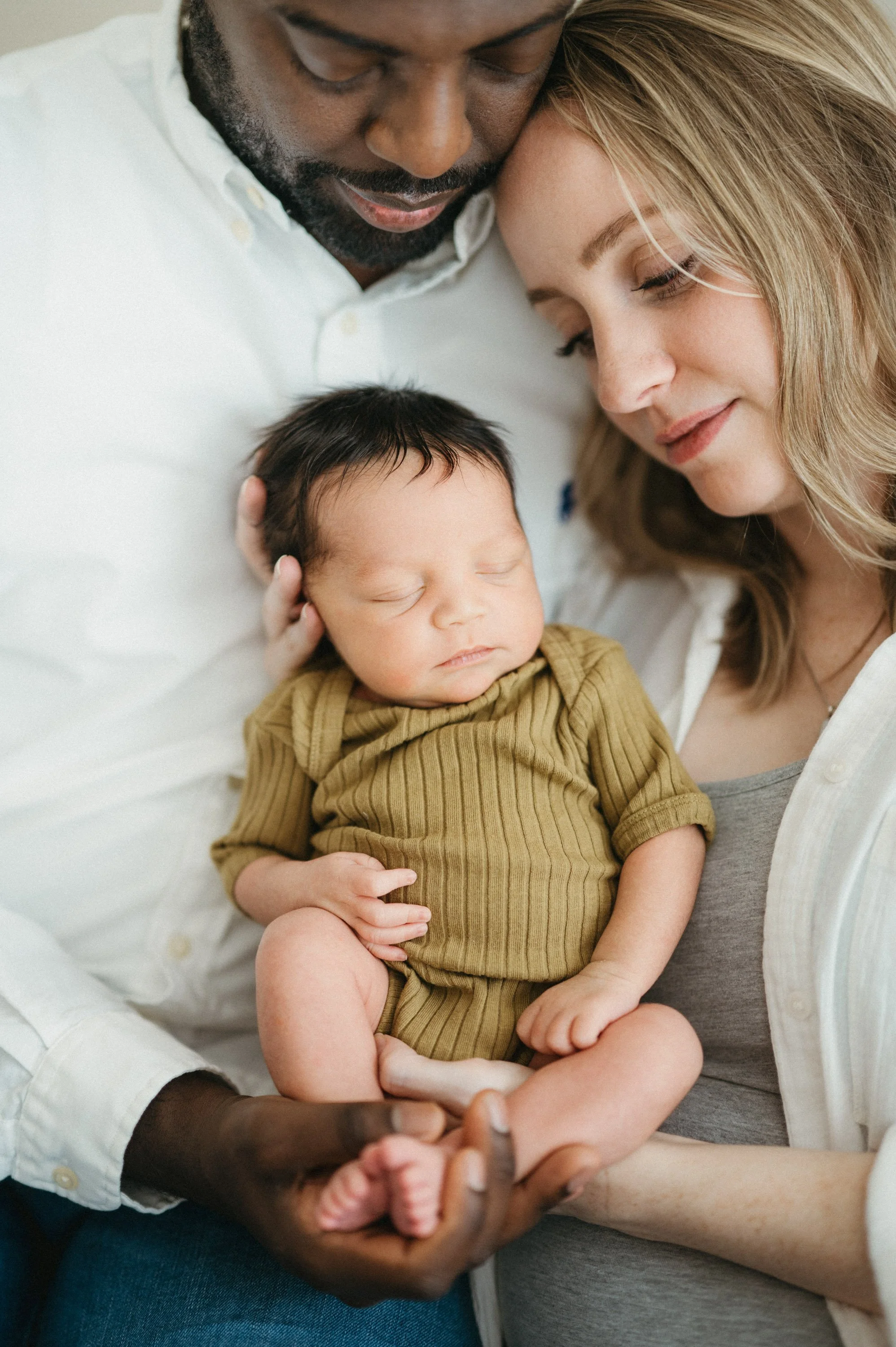 Close-up of a man and woman tenderly holding a sleeping baby together.