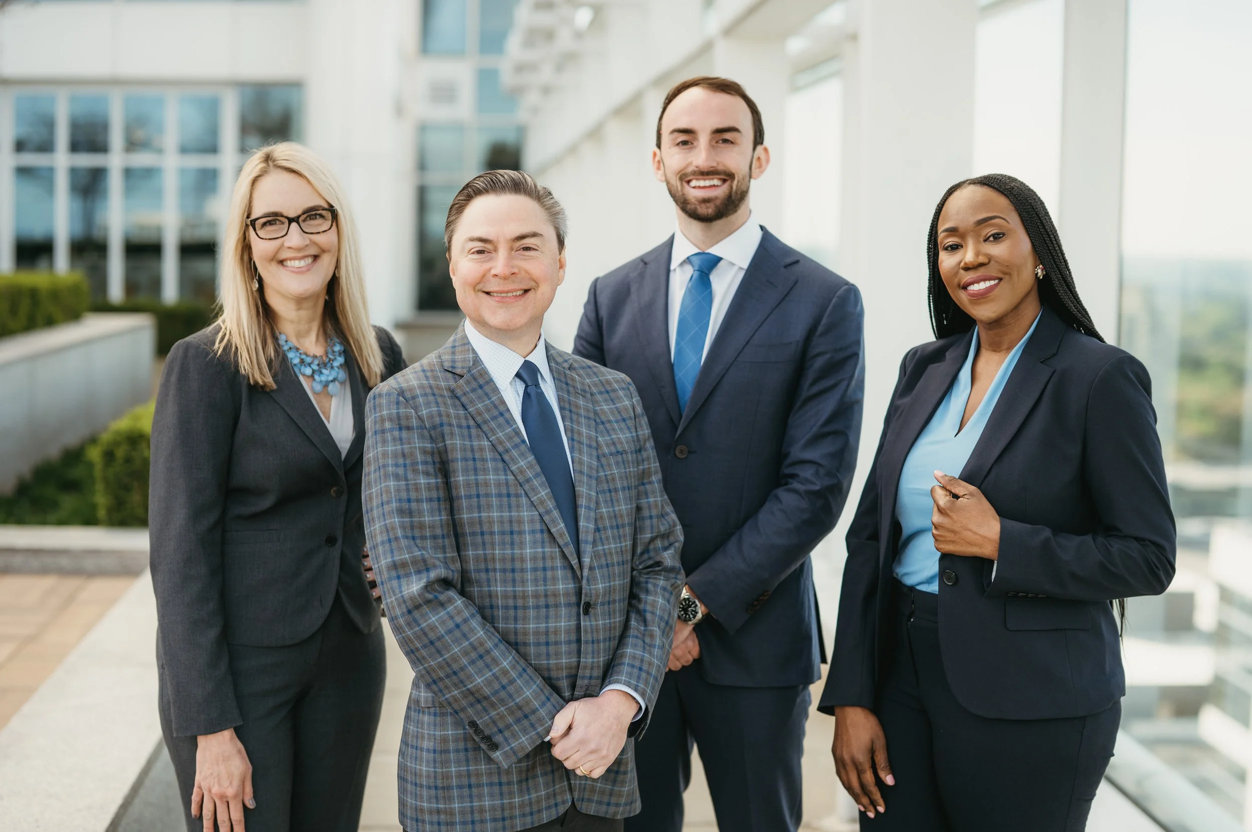 Four professionally dressed people smiling and posing outside a modern office building.