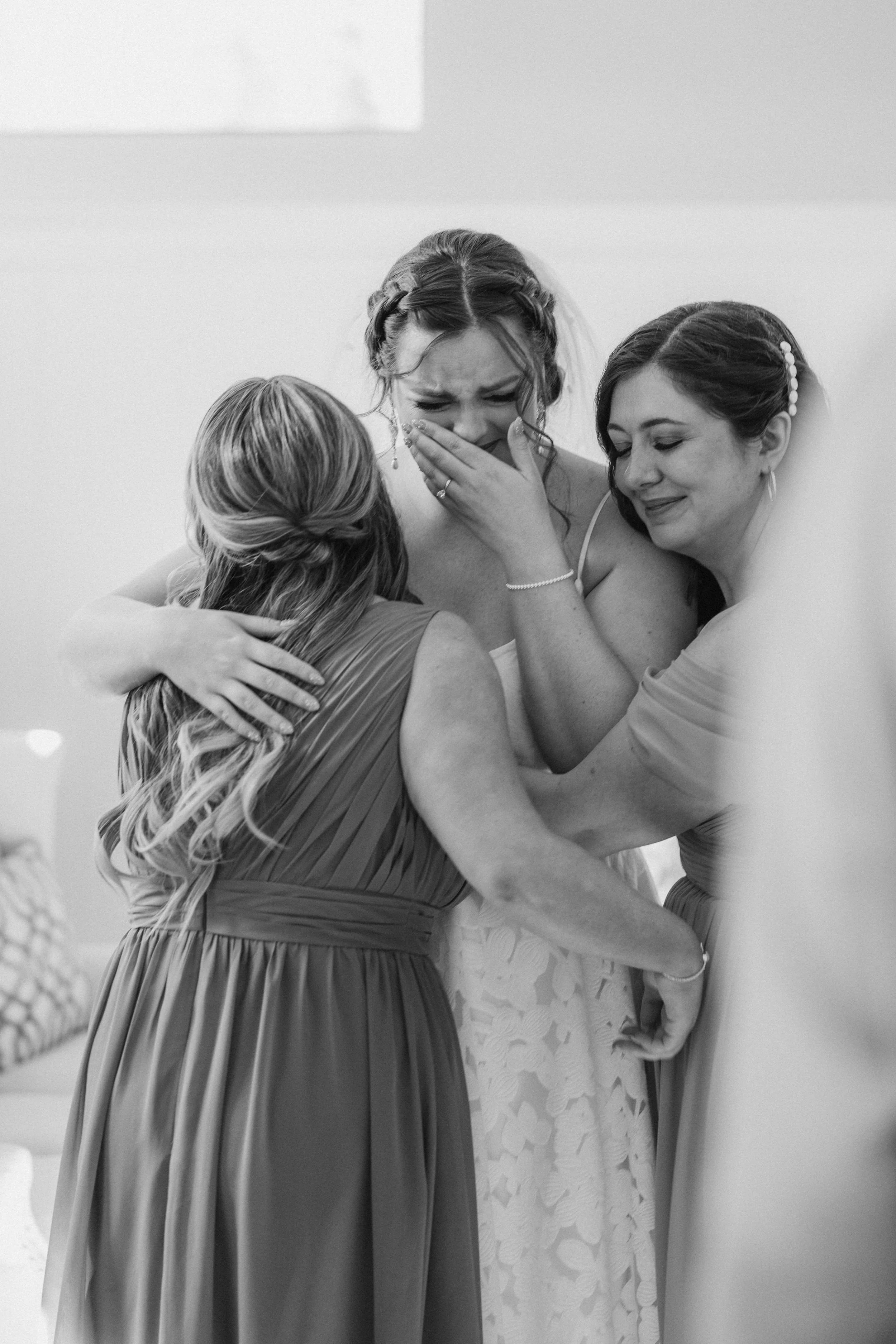 Three women sharing an emotional moment, with one woman crying and others comforting her, at a wedding or special event.